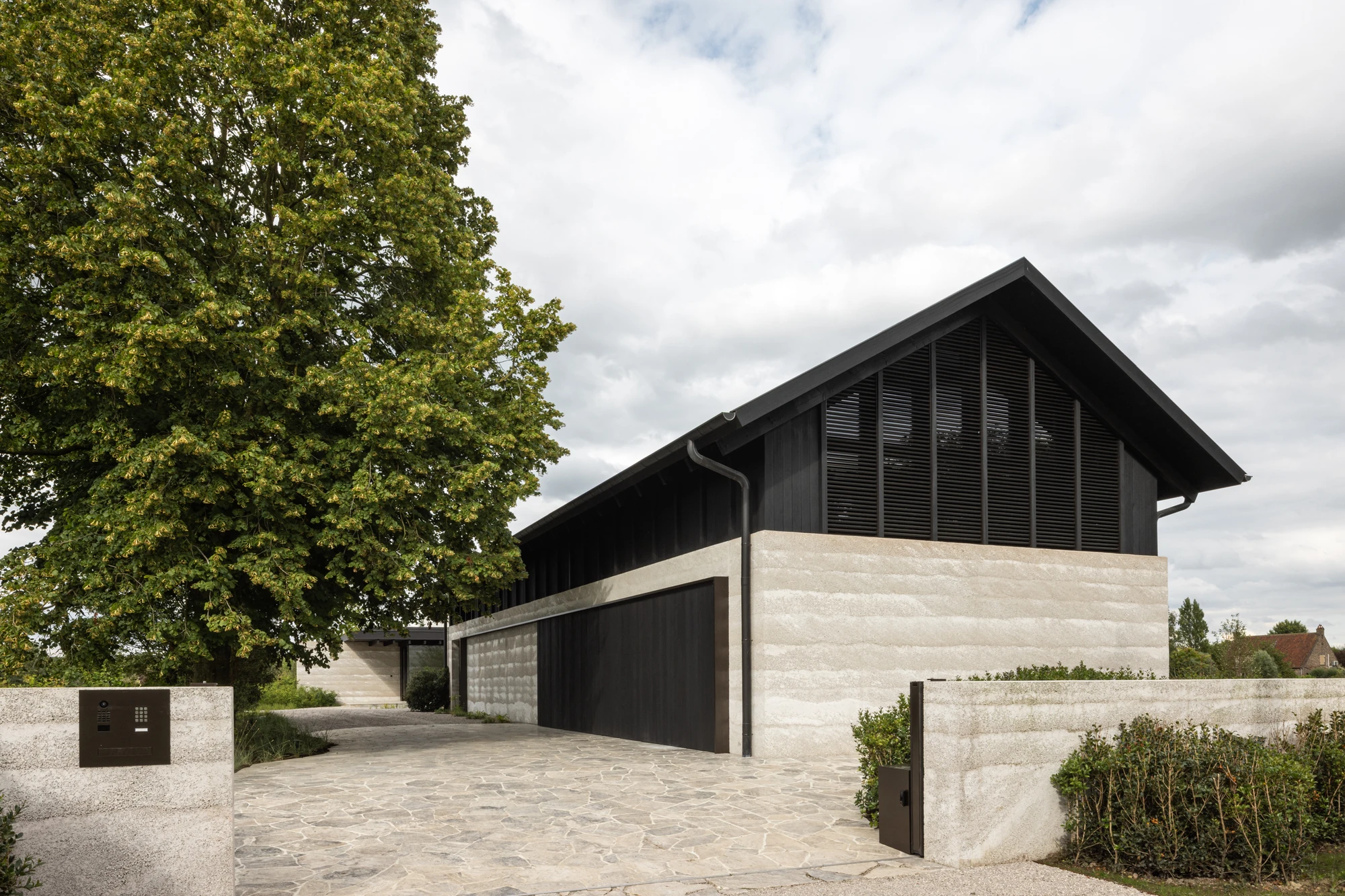 Villa WIGO by CAS Architecten — A rendered concrete perimeter wall frames the approach to Villa WIGO, its smooth pale surface punctuated by a recessed entrance gate and integrated planting.