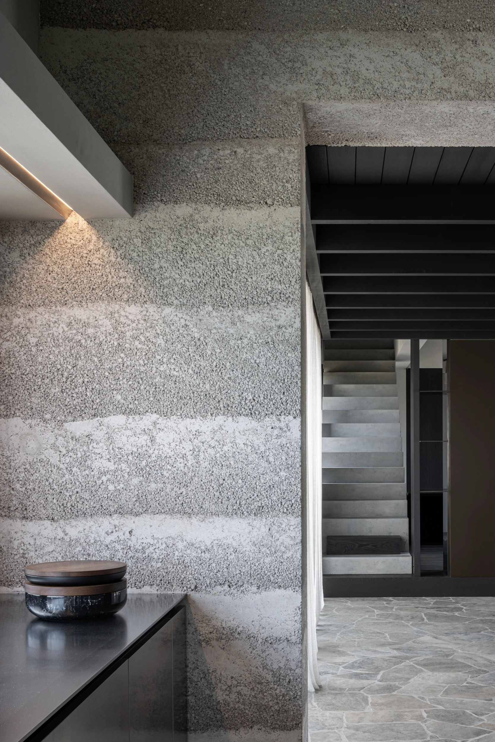 Villa WIGO by CAS Architecten — A concrete staircase descends through the L-shaped villa, its monolithic board-formed walls displaying horizontal striations and weathered surface patina.