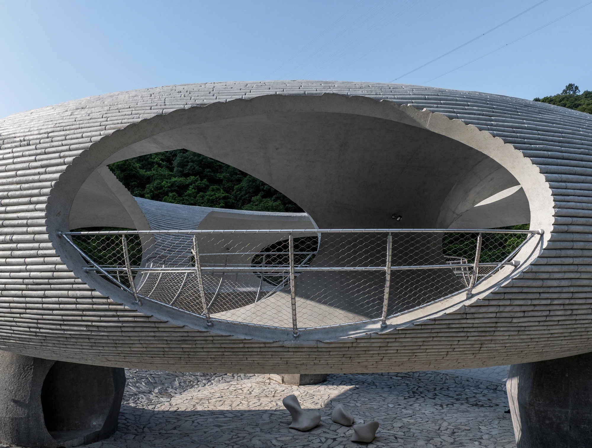 Resting Loop with Views by HCCH Studio — A concrete ring structure frames dense forest canopy through a large elliptical aperture, with a stainless steel cable railing running along the curved...