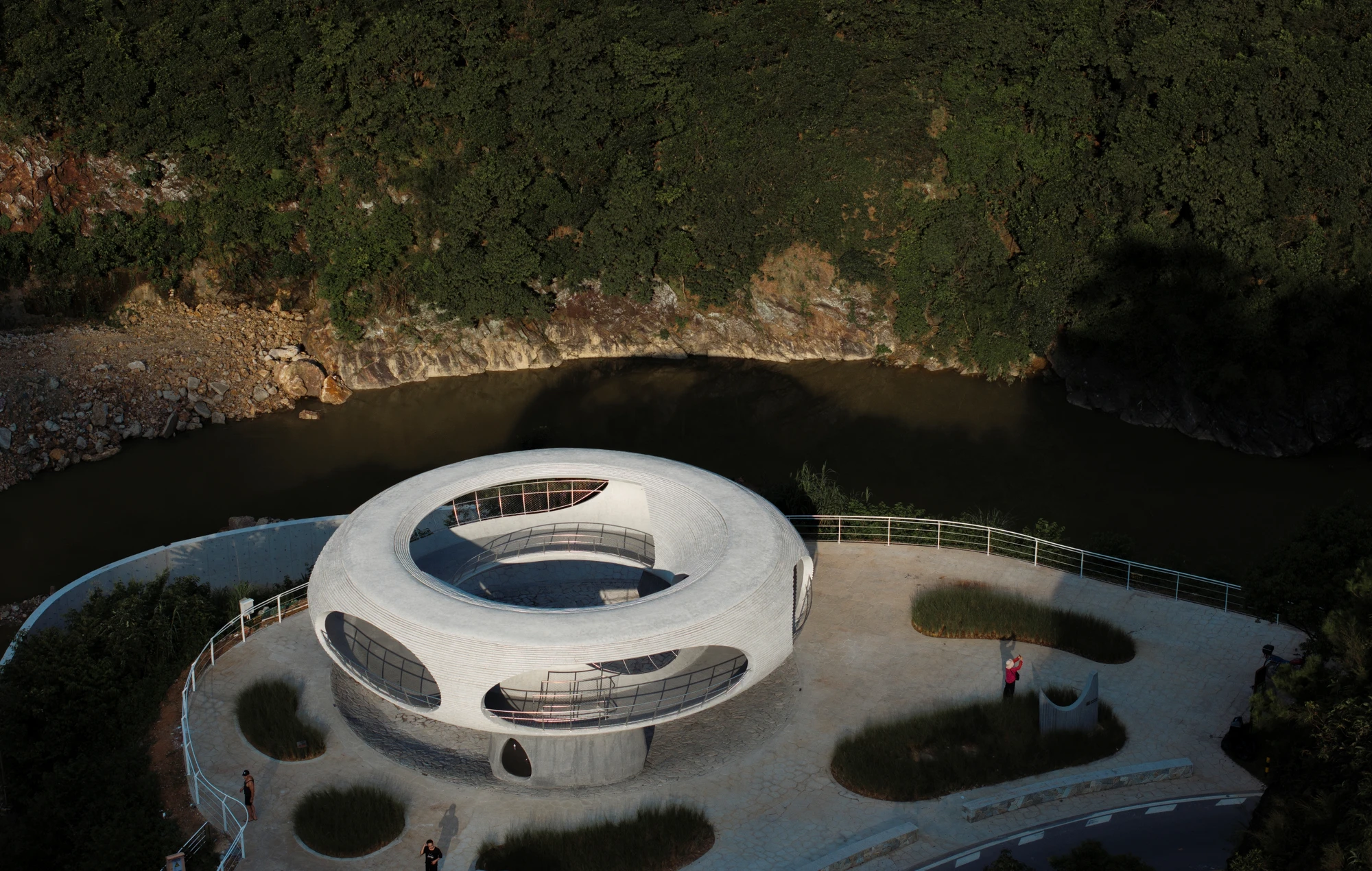 Resting Loop with Views by HCCH Studio — Aerial view of a monolithic concrete ring structure positioned on a stone platform overlooking a river valley.