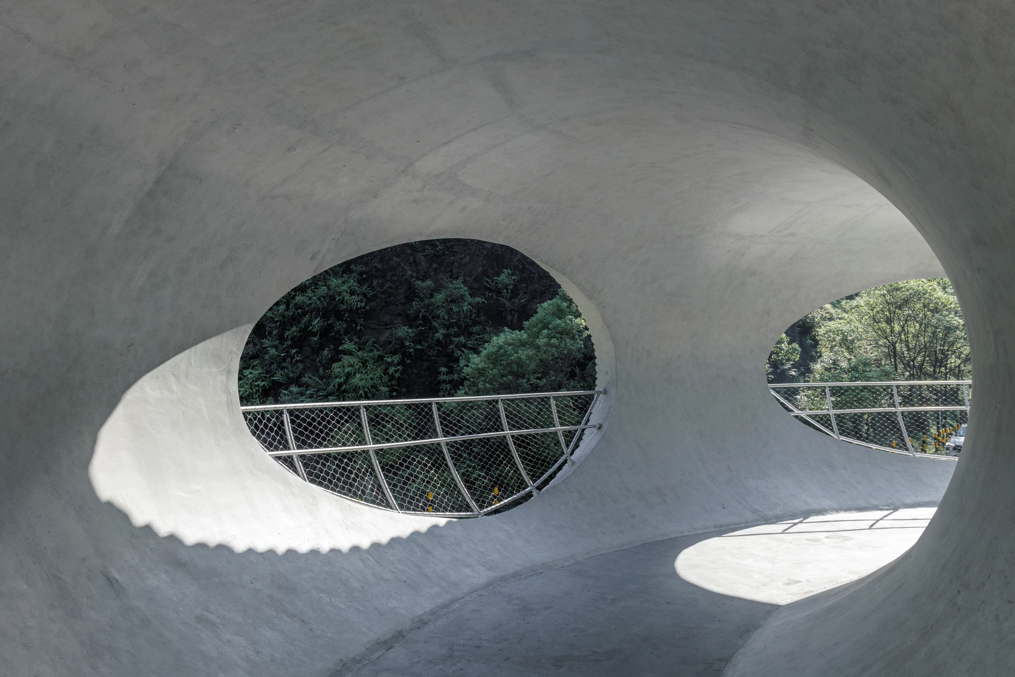 Resting Loop with Views by HCCH Studio — Two oval apertures cut through the monolithic concrete ring, framing layered views of dense forest canopy in sharp focus.