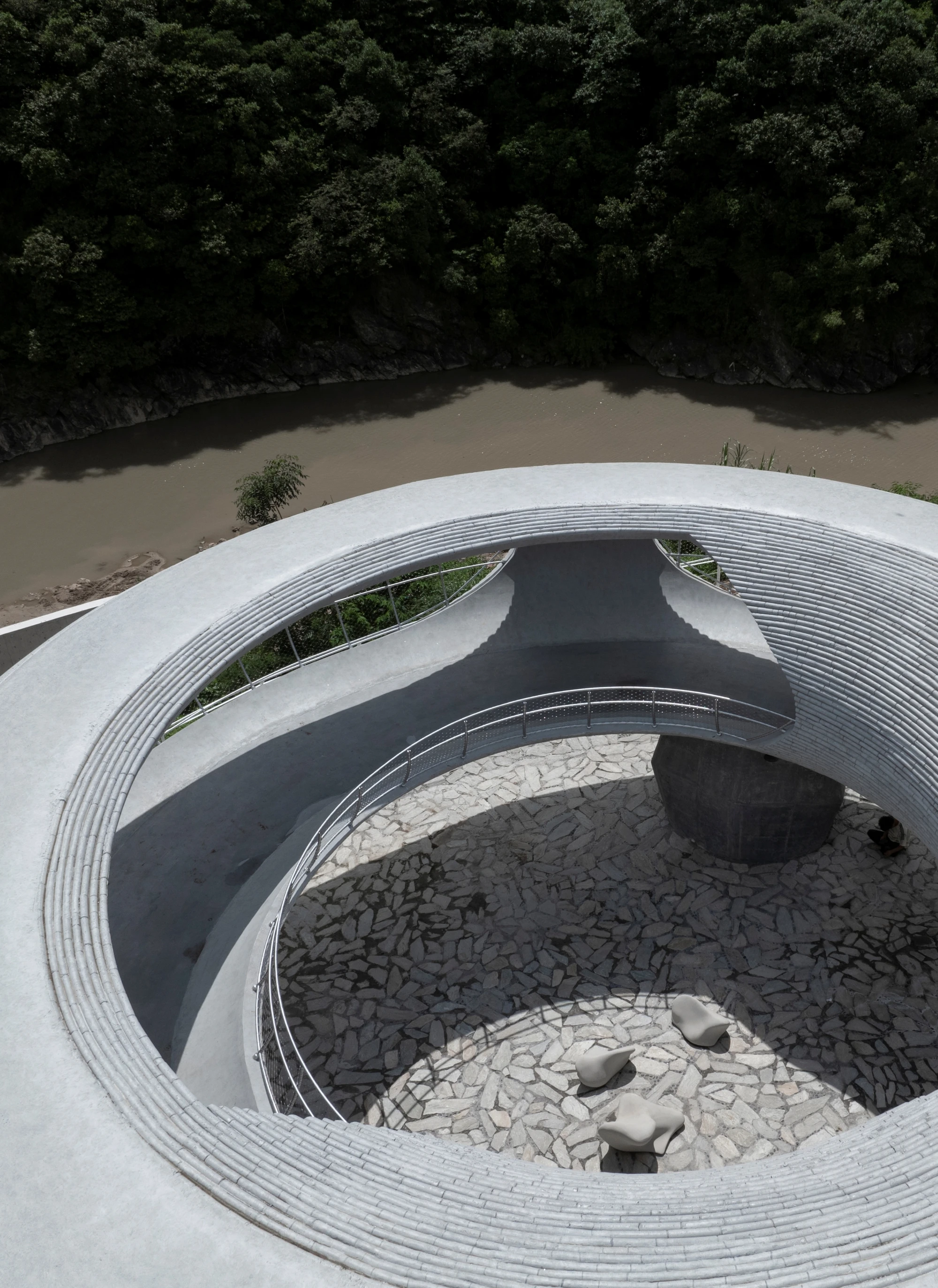 Resting Loop with Views by HCCH Studio — Aerial perspective reveals the concrete ring's internal geometry, where stacked stone platforms in grey and cream create a sectional descent into the...