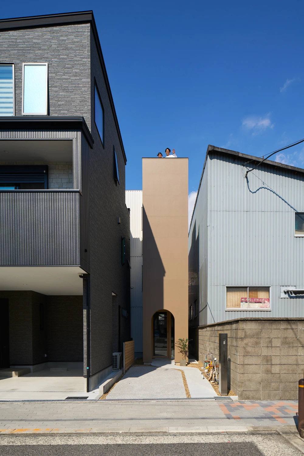House in Hirano by Fujiwaramuro Architects — A peach-rendered facade rises between darker neighboring structures on an Osaka flagpole lot, its uninterrupted vertical surface broken only by an arched...