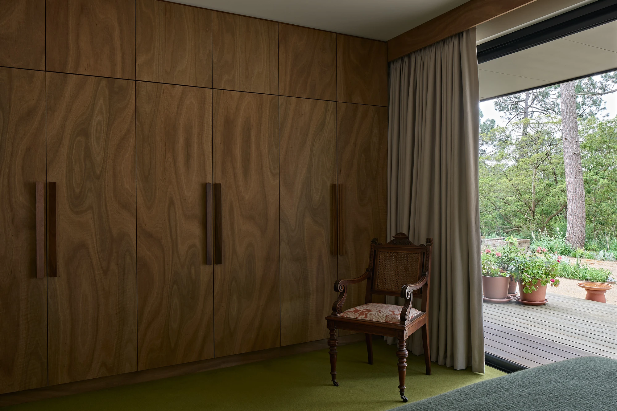 Homestead House by MRTN Architects — A bedroom interior dominated by a walnut-veneered wardrobe system with recessed pulls, occupying the full wall plane.