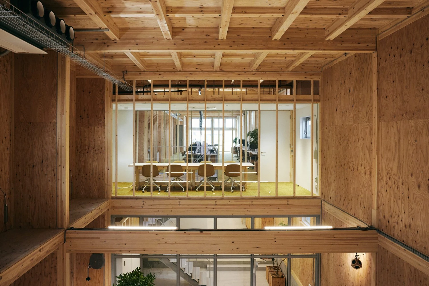 Uchida Shoten Head Office by Jo Nagasaka / Schemata Architects — Interior view across two stories of timber-framed office space, shot from an upper-floor corridor looking toward an open-plan work area.