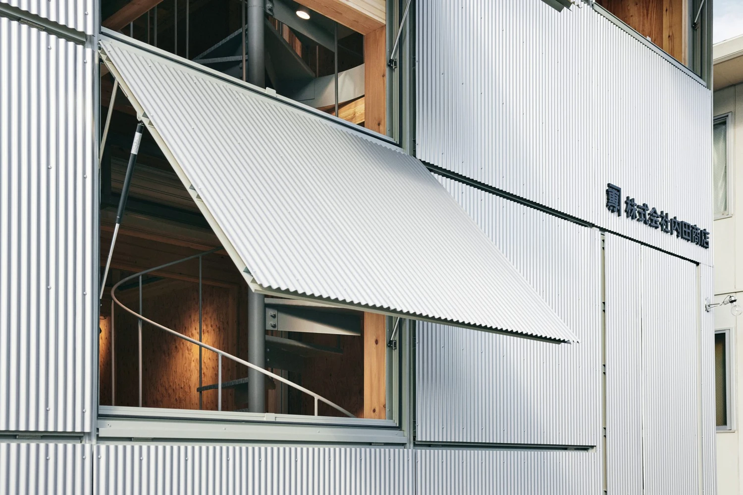 Uchida Shoten Head Office by Jo Nagasaka / Schemata Architects — A diagonal corrugated metal awning extends from the white-clad facade, its hinged edge sharp against the sky.