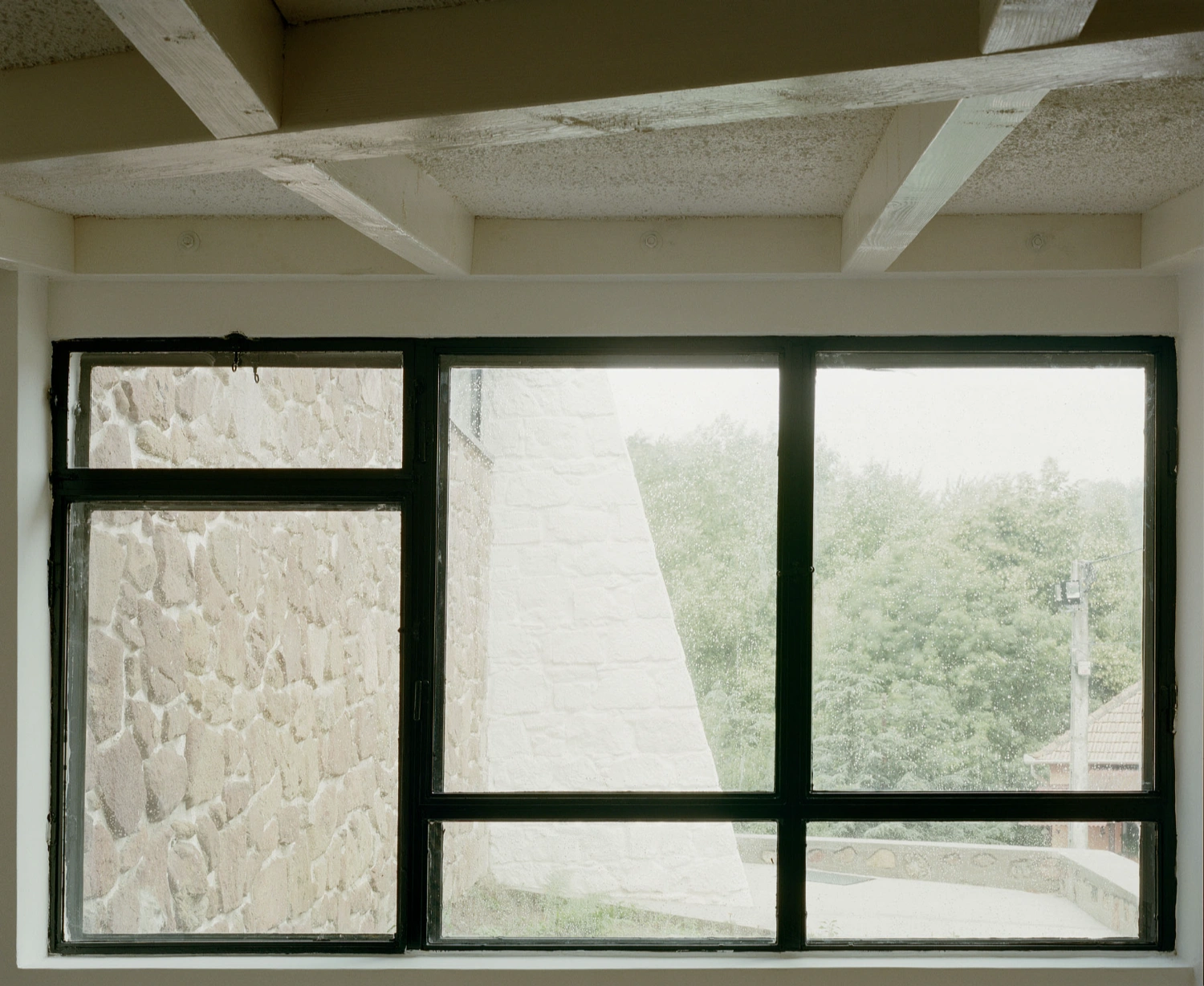 Restoration of the Church of Cserépváralja by Partizan Architecture — A gridded window system with dark steel framing divides the view into six panes, set into the church's rendered stone wall.