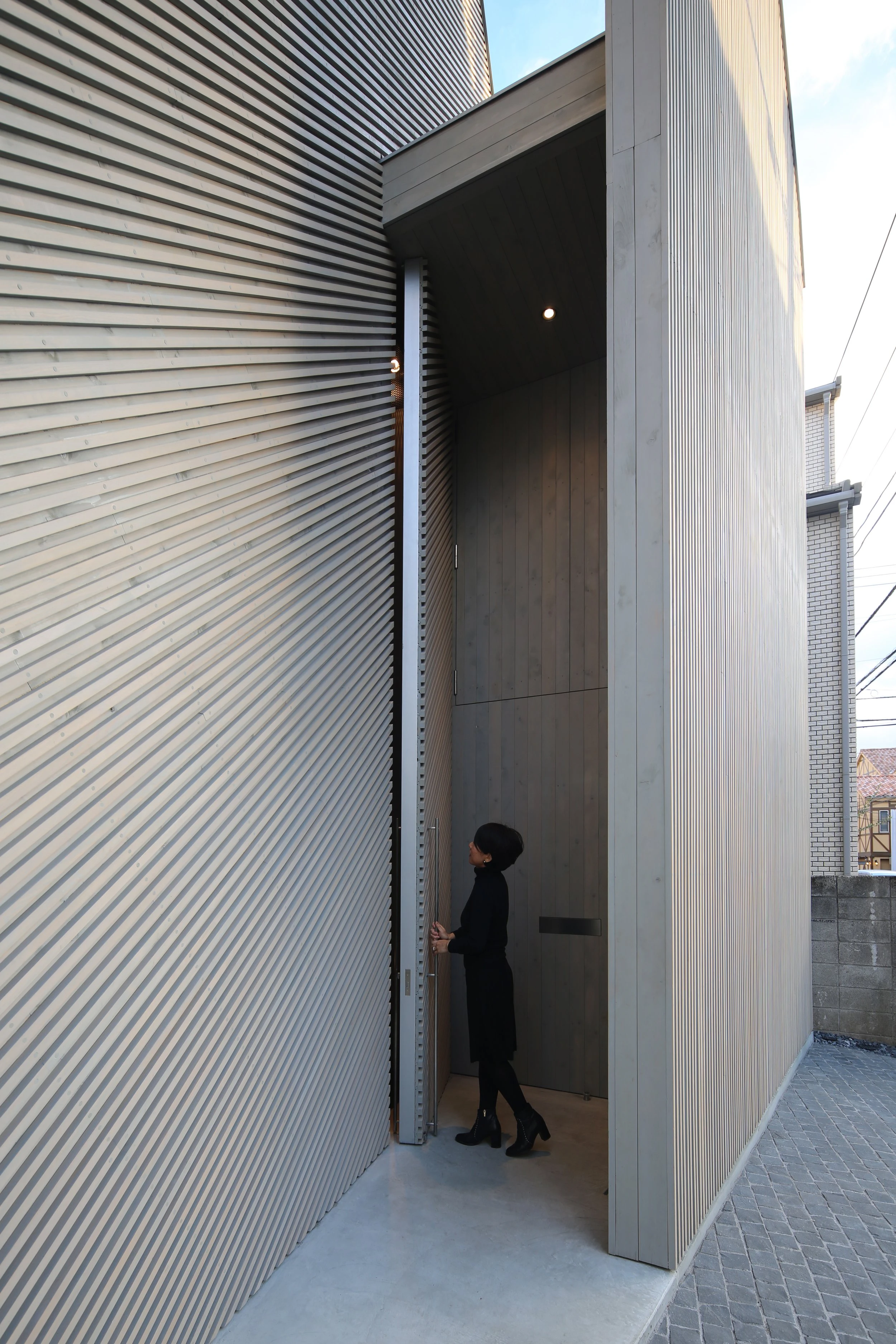 Music Hall in the Sky by Takuro Yamamoto Architects — A narrow passage reveals the entrance sequence to the concert hall, where corrugated metal cladding in light grey forms the left wall, creating strong...