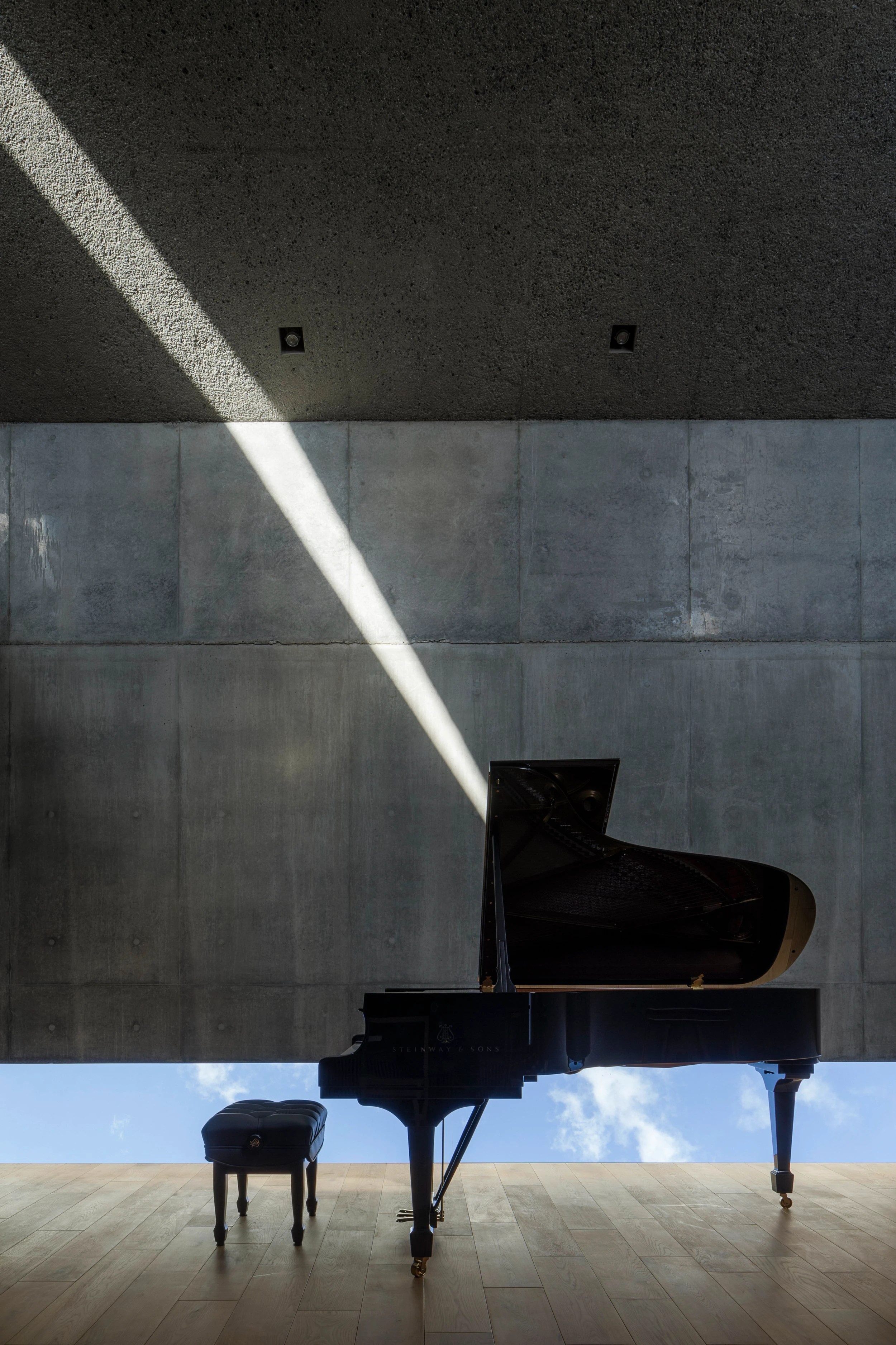 Music Hall in the Sky by Takuro Yamamoto Architects — A grand piano occupies the center of this 50-seat concert hall, positioned directly beneath a diagonal skylight that bisects the concrete interior.