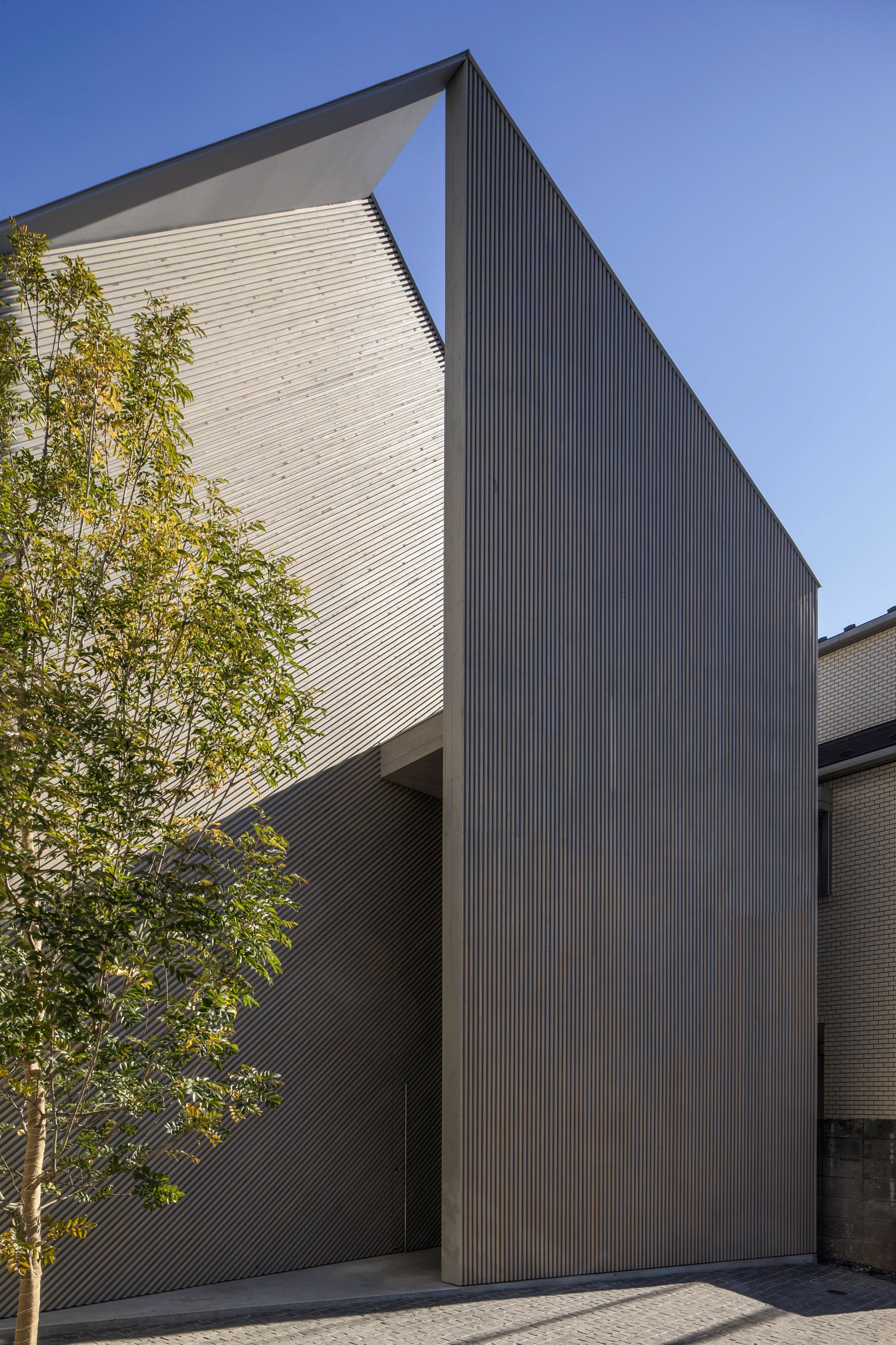 Music Hall in the Sky by Takuro Yamamoto Architects — The monolithic facade of Music Hall in the Sky presents a gridded vertical corrugated metal surface in charcoal, rising sharply against clear sky.