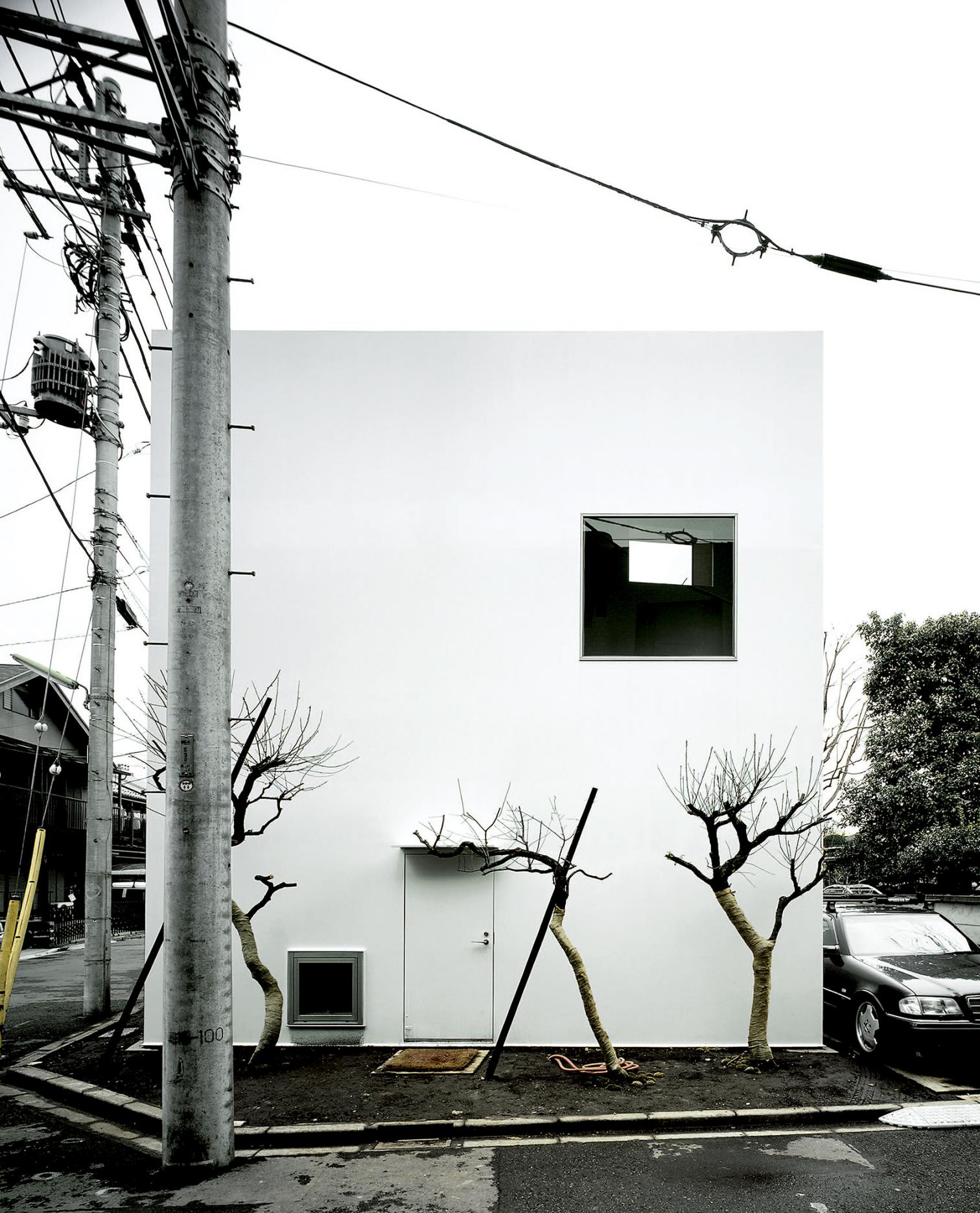 House in a Plum Grove by Kazuyo Sejima by Kazuyo Sejima & Associates — A rendered white facade compressed between neighboring structures on a Tokyo corner plot, its geometric clarity disrupted by organic intervention.