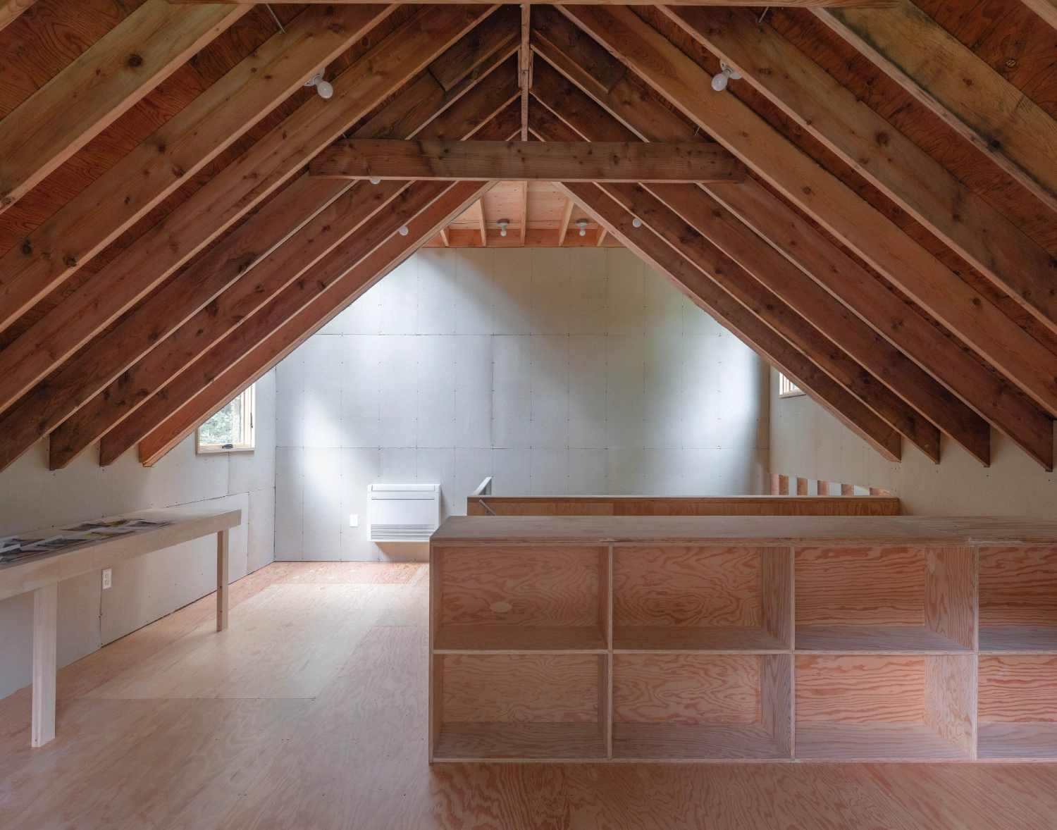 Studio Barn by Worrell Yeung — An unfinished studio barn interior reveals the structural skeleton of exposed timber rafters and beams in honey-colored wood.