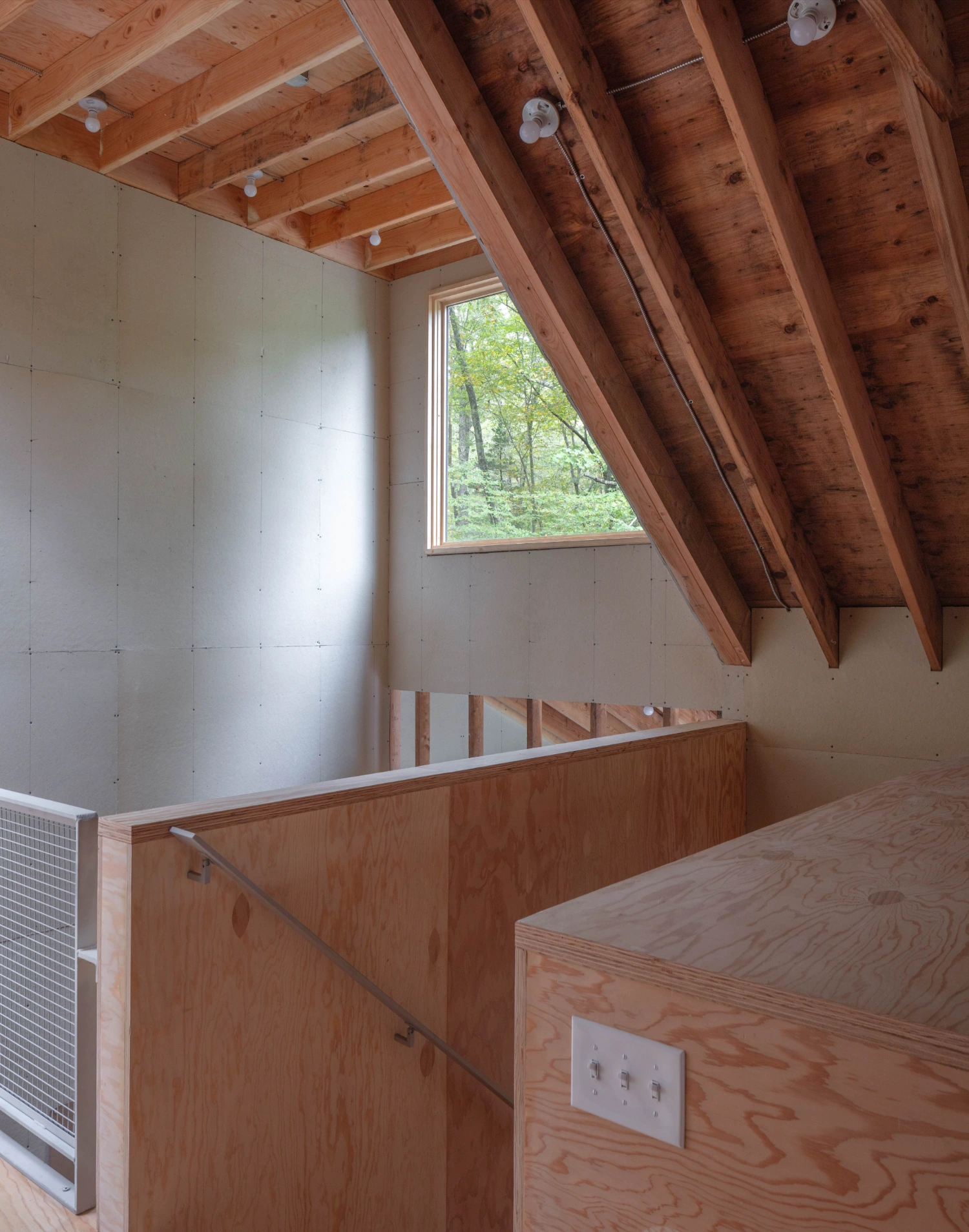 Studio Barn by Worrell Yeung — Interior view of the Studio Barn's mezzanine level, capturing exposed timber roof beams with visible knots and patina against pale drywall.
