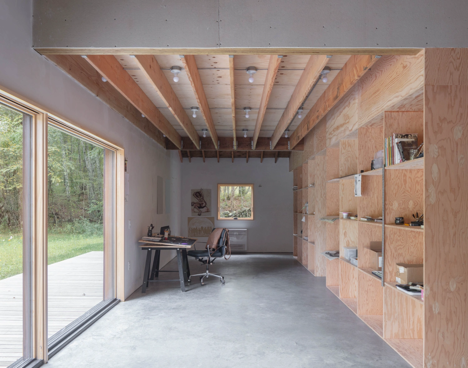 Studio Barn by Worrell Yeung — A timber-framed studio interior in Rhode Island reveals exposed wooden beams across the ceiling and plywood storage cabinetry lining the right wall.