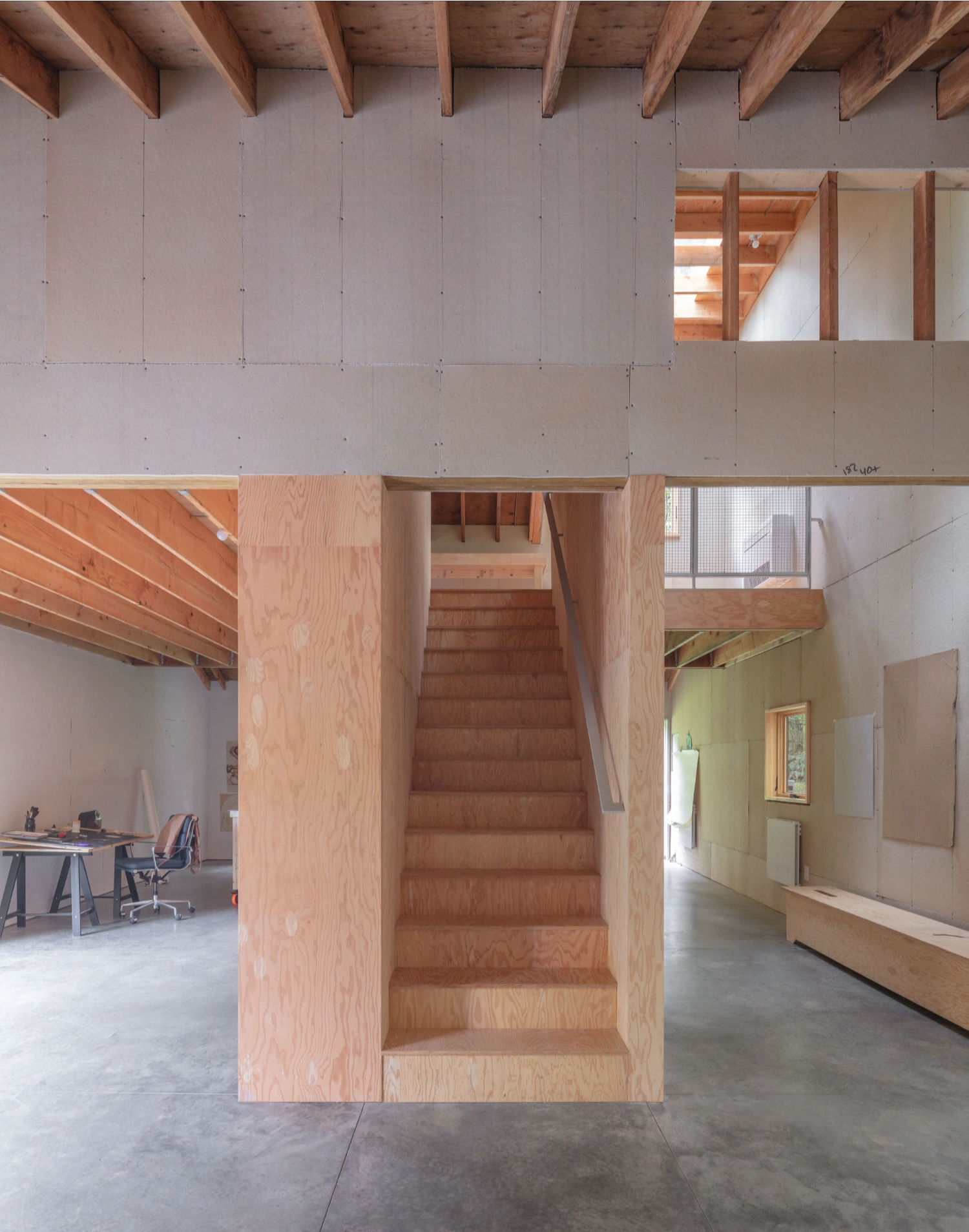 Studio Barn by Worrell Yeung — A central timber staircase dominates the open-plan interior, its plywood construction revealing the building's skeletal framework.