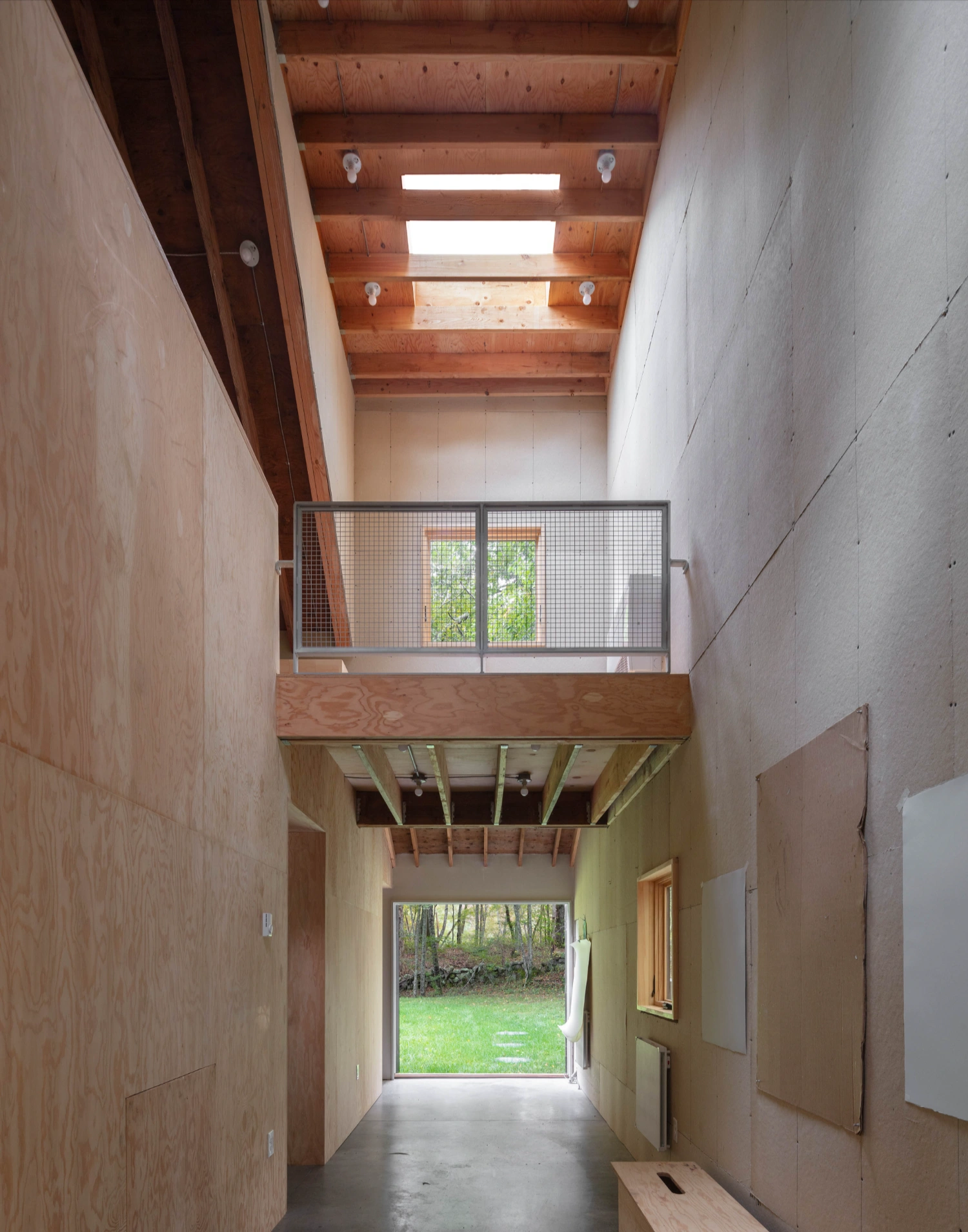 Studio Barn by Worrell Yeung — A double-height corridor in Studio Barn reveals the post-and-beam timber structure overhead, with exposed wooden joists and white skylights introducing...