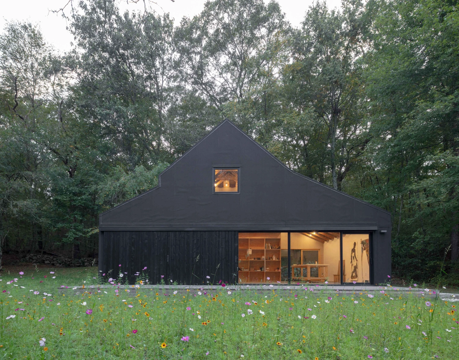 Studio Barn by Worrell Yeung — A black-clad barn structure with pitched roof sits within a wildflower meadow dotted with purple, yellow, and white blooms.