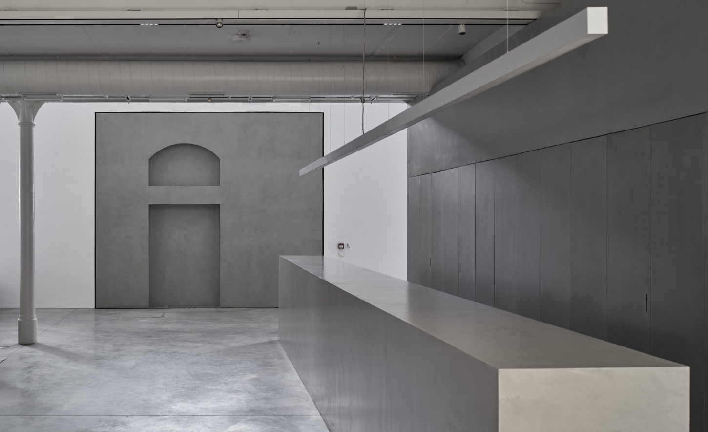 PLATO Contemporary Art Gallery by KWK PROMES — A monolithic concrete pavilion with sharp rectilinear edges inserted into the gallery's interior, its pristine grey surface creating stark material contrast...
