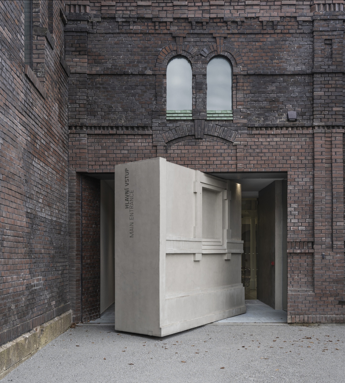 PLATO Contemporary Art Gallery by KWK PROMES — A micro-concrete pavilion with sharp rectilinear geometry occupies the brick threshold of the gallery entrance.