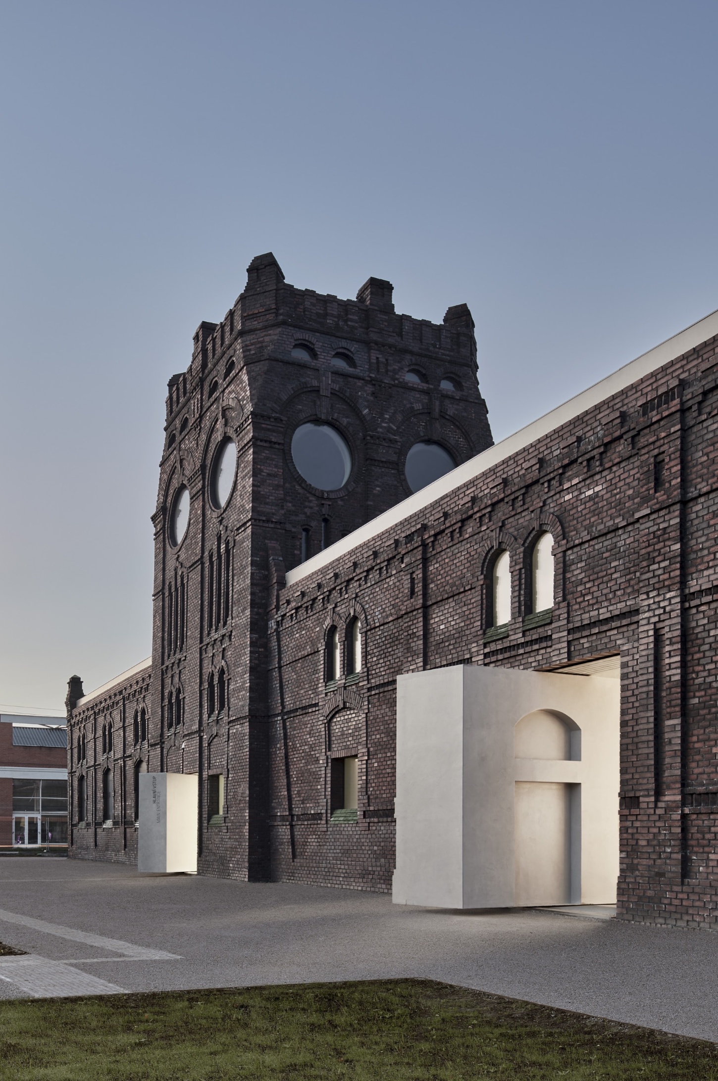 PLATO Contemporary Art Gallery by KWK PROMES — A micro-concrete pavilion with sharp rectilinear geometry punctuates the brick courtyard, its white surfaces creating stark material contrast against the...