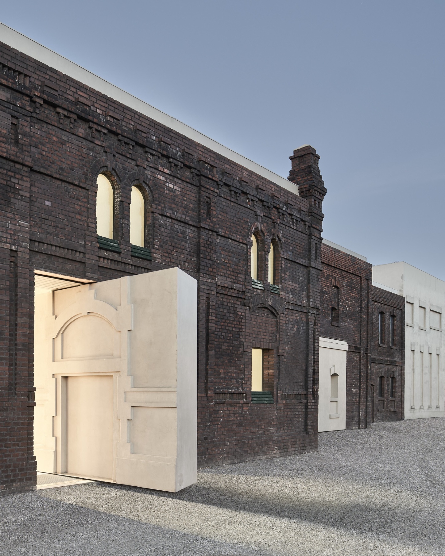 PLATO Contemporary Art Gallery by KWK PROMES — A cream-colored concrete pavilion with sharp rectilinear geometry protrudes into the brick facade of the original industrial building.