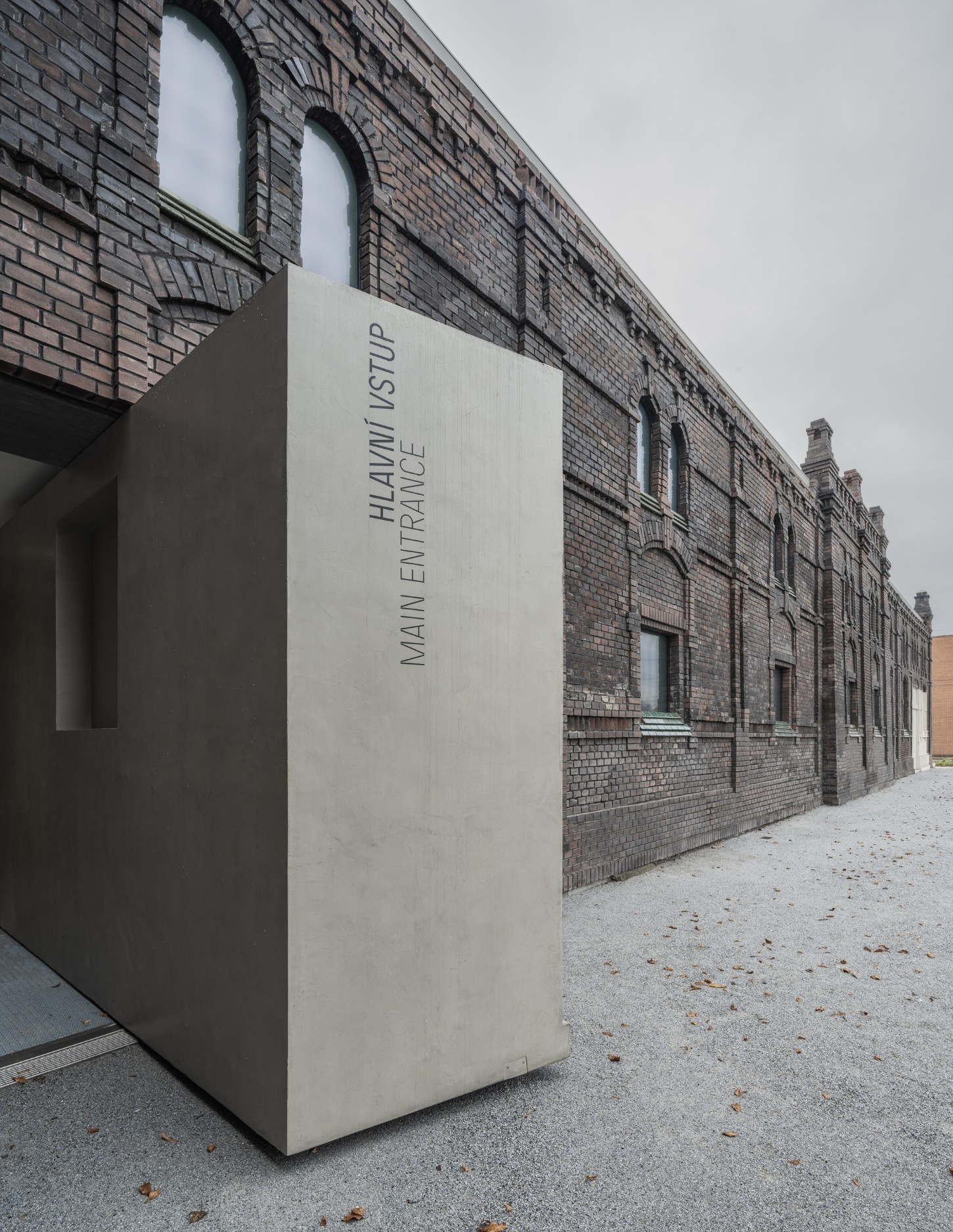 PLATO Contemporary Art Gallery by KWK PROMES — A monolithic concrete pavilion with sharp rectilinear geometry protrudes from the brick facade of the gallery's main entrance.