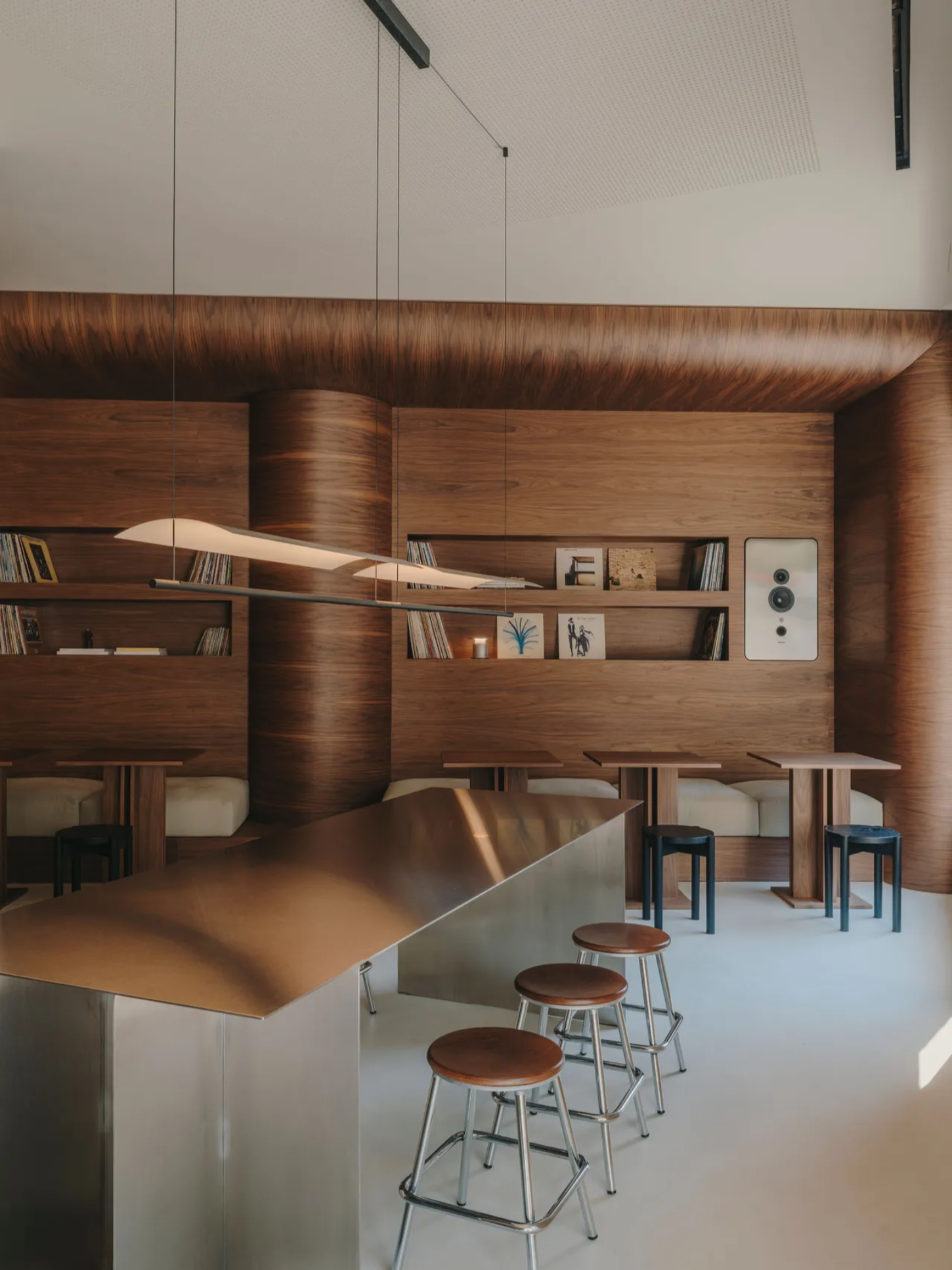 Jaç Hi-fi Cafe by Isern Serra — The Jaç Hi-fi Cafe interior showcases a continuous walnut grain treatment flowing from integrated wall shelving through curved ceiling paneling, creating a...