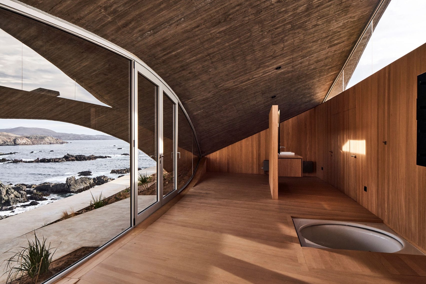 A wave-like roof curves over Los Vilos house by Ryue Nishizawa, blending structure with the cliff concrete architecture