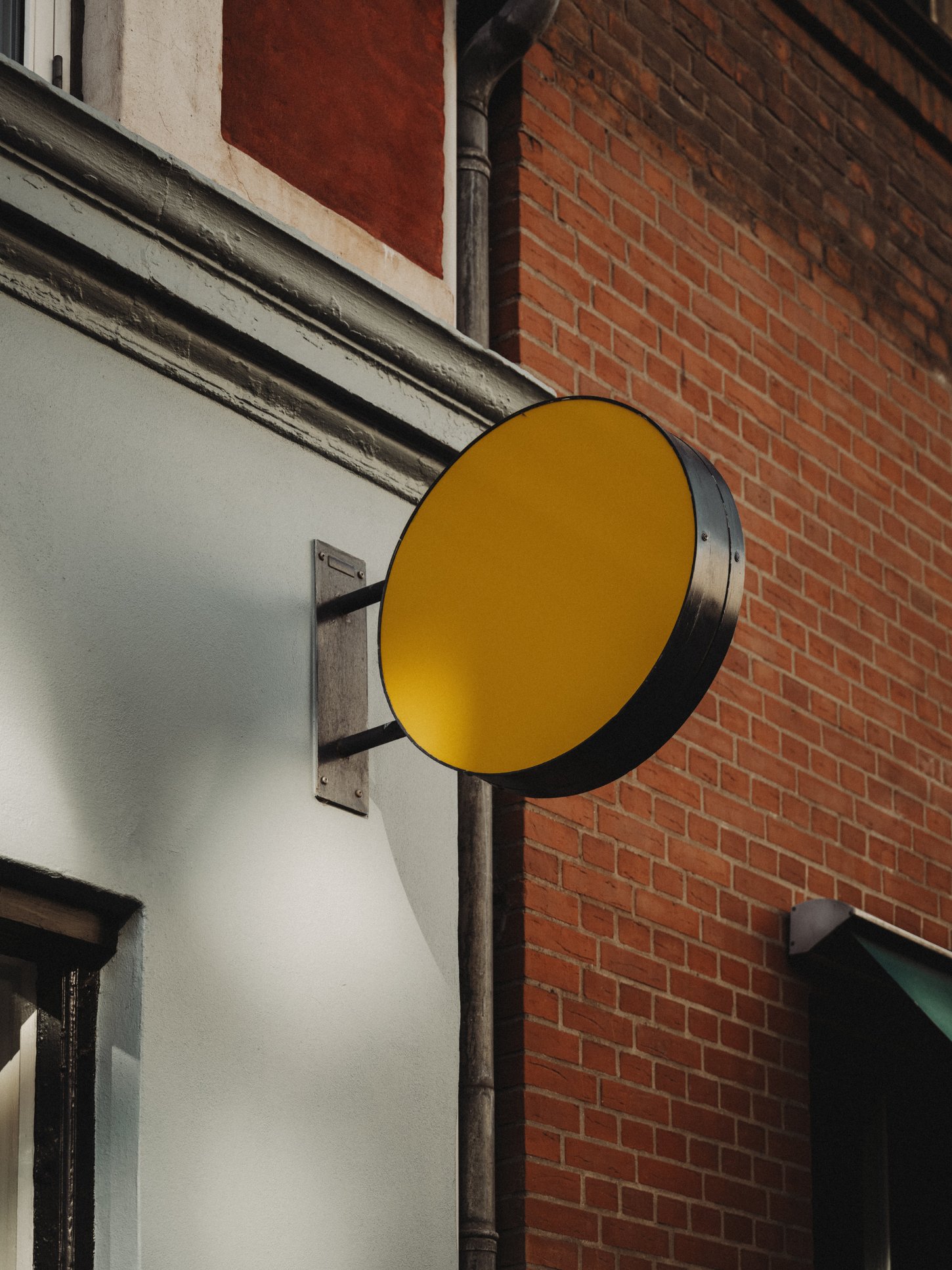 Amator Restaurant by wiercinski-studio — A bright yellow circular signage element mounted on a weathered steel bracket projects perpendicular from the building facade, creating a bold graphic...