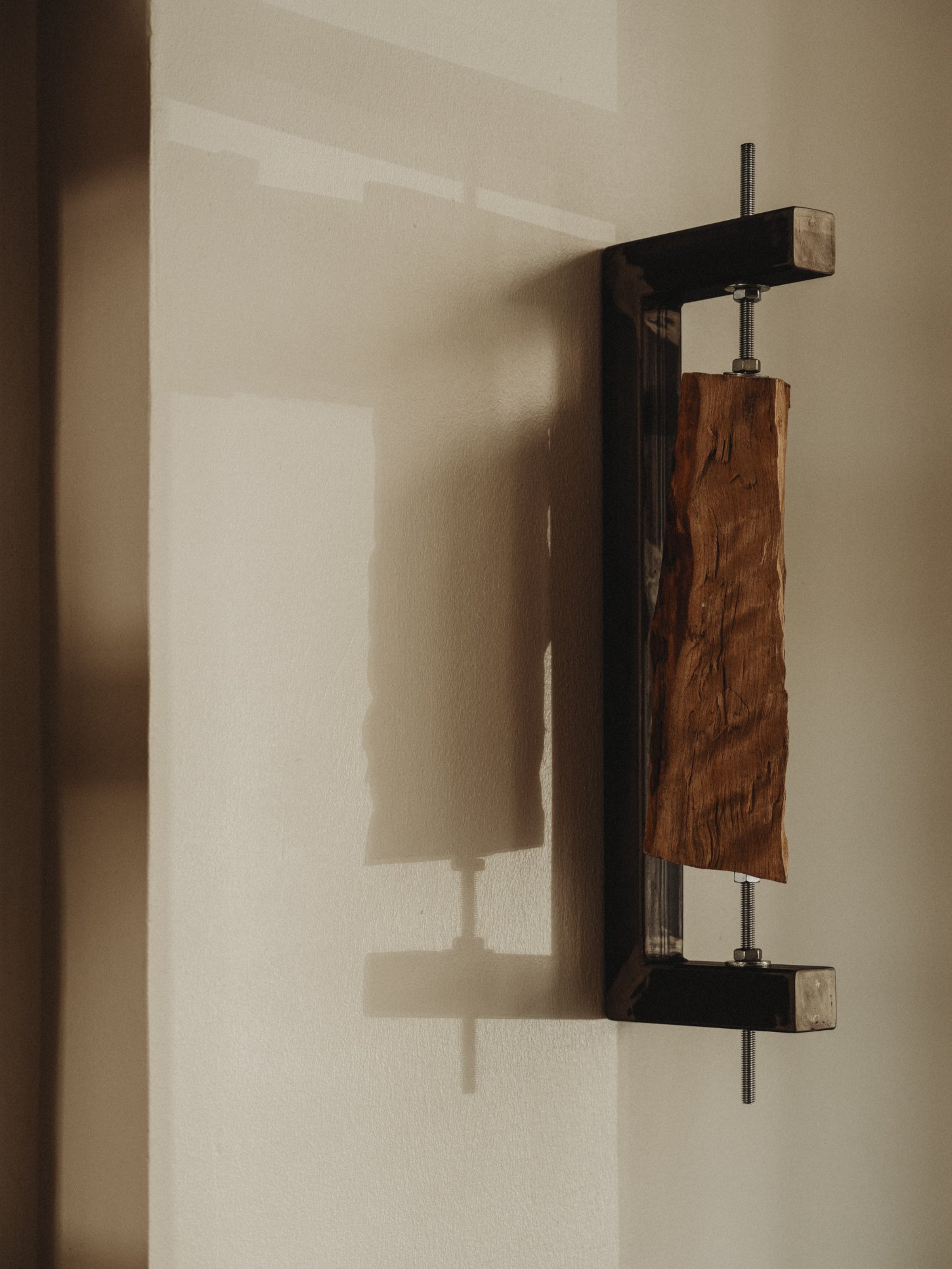 Amator Restaurant by wiercinski-studio — A sculptural wooden clamp mounted vertically on a cream-colored wall, constructed from dark-stained timber frames with a rich walnut-toned wood block held...