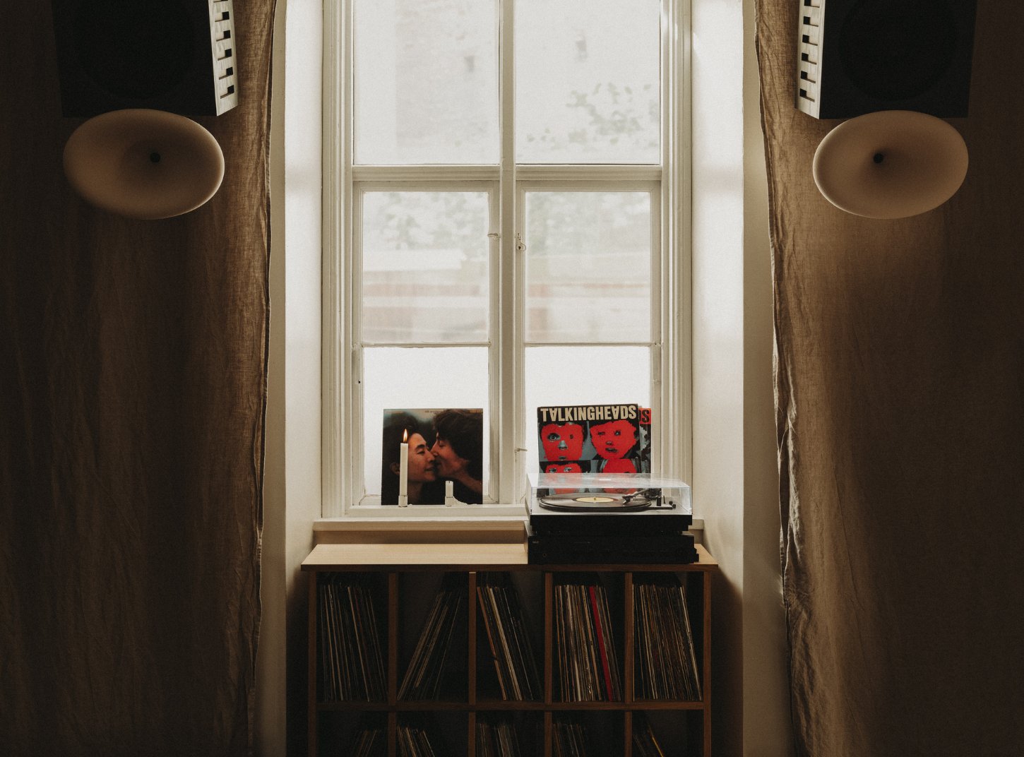 Amator Restaurant by wiercinski-studio — A window-facing record storage installation framed by brown linen curtains and flanked by two ceramic pendant lights.