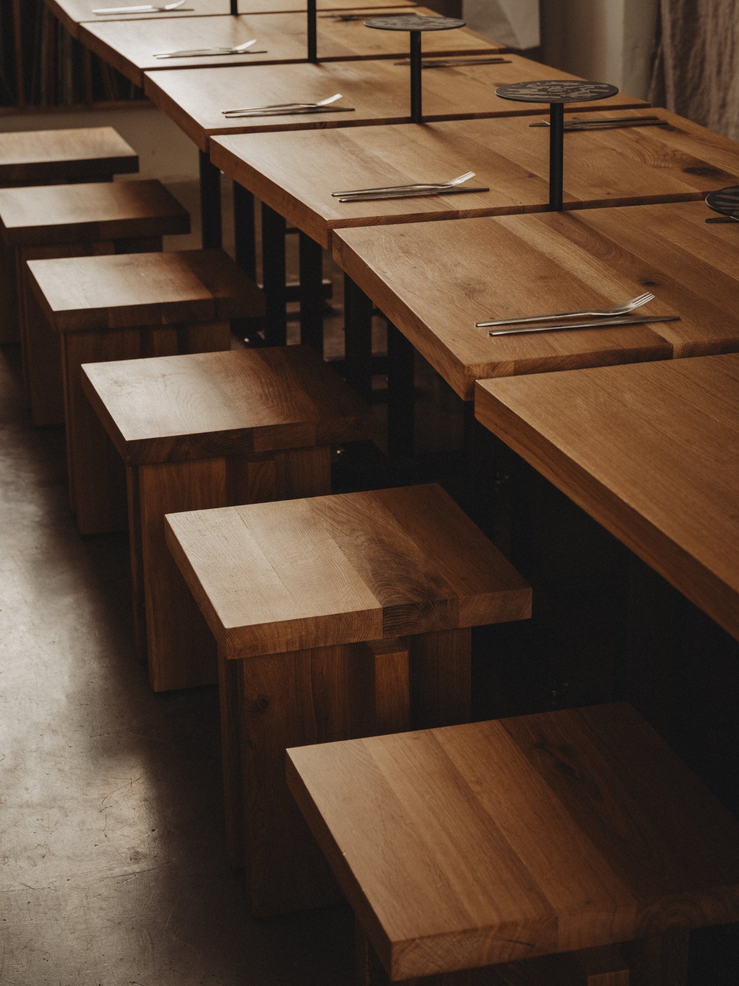 Amator Restaurant by wiercinski-studio — Solid oak benches with light-finished tops recede into depth, their jagged edges creating angular rhythm across the dining space.