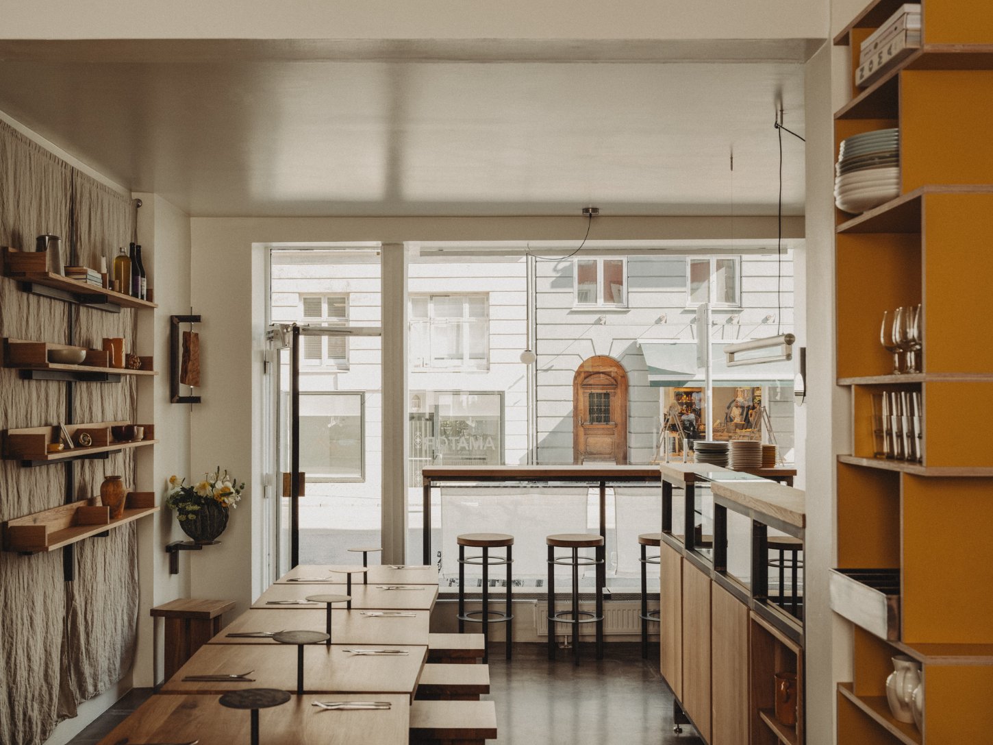 Amator Restaurant by wiercinski-studio — The dining room unfolds in receding perspective, with solid oak benches arranged in staggered alignment along a dark steel-framed counter.