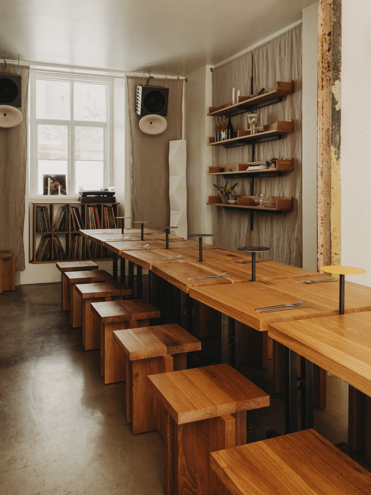 Amator Restaurant by wiercinski-studio — The dining room features a linear arrangement of solid oak benches with light-finished tops positioned in receding perspective down the length of the space.
