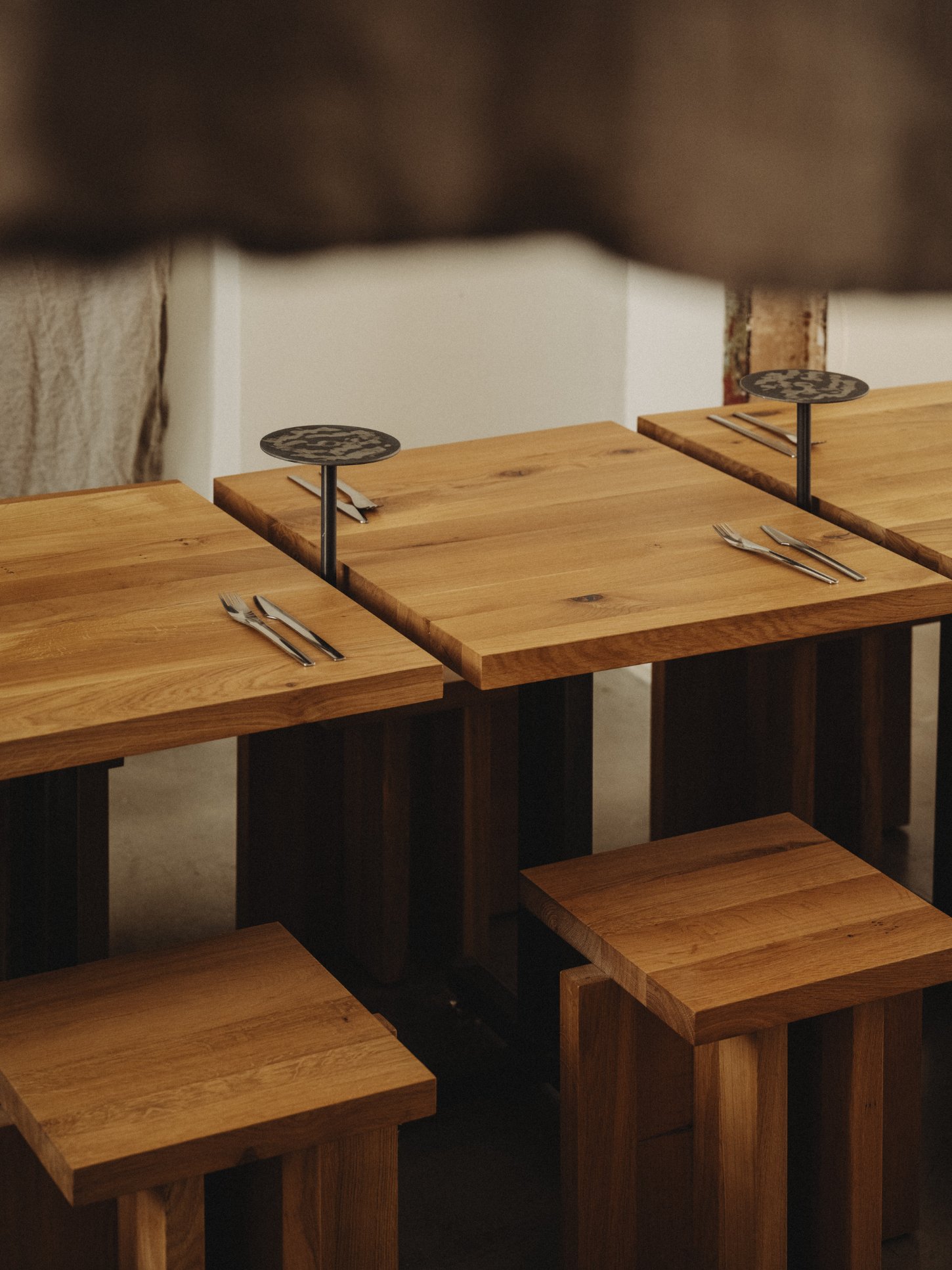 Amator Restaurant by wiercinski-studio — Solid oak dining tables with light-finished tops arranged in receding perspective, their edges cut at jagged angles creating visual rhythm across the space.