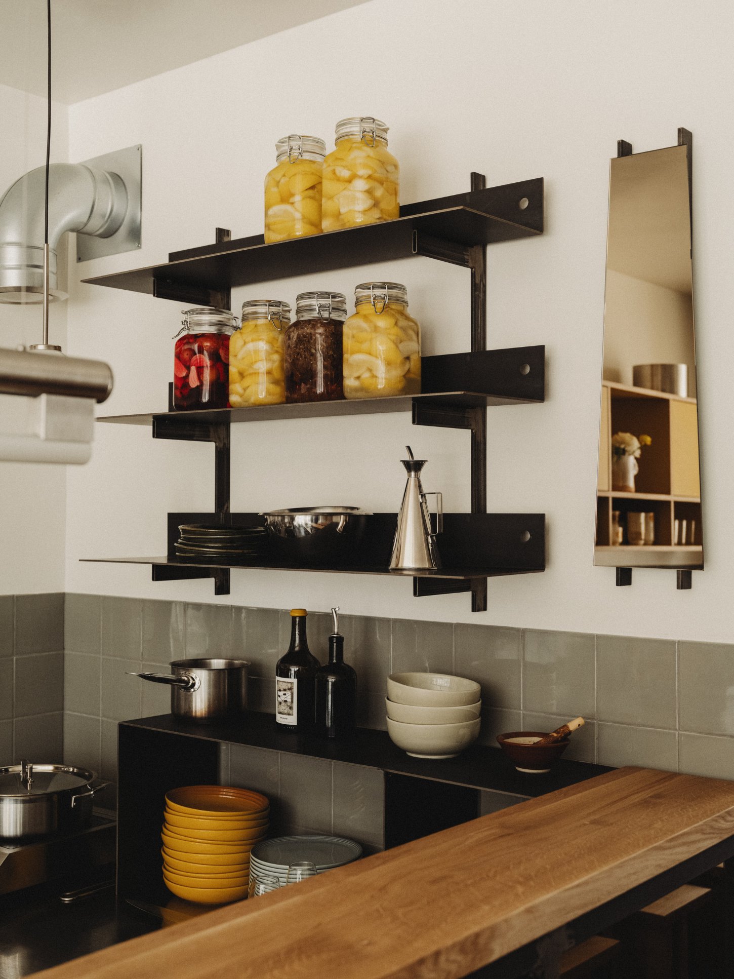 Amator Restaurant by wiercinski-studio — A kitchen wall organization system featuring three black steel cantilever shelves mounted to white plaster.