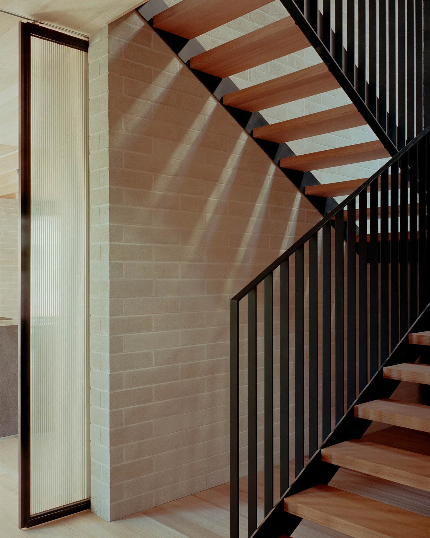 Echo House by Parabolica — A cantilever timber staircase with warm-toned wood treads and underside faces descends past a black metal balustrade.