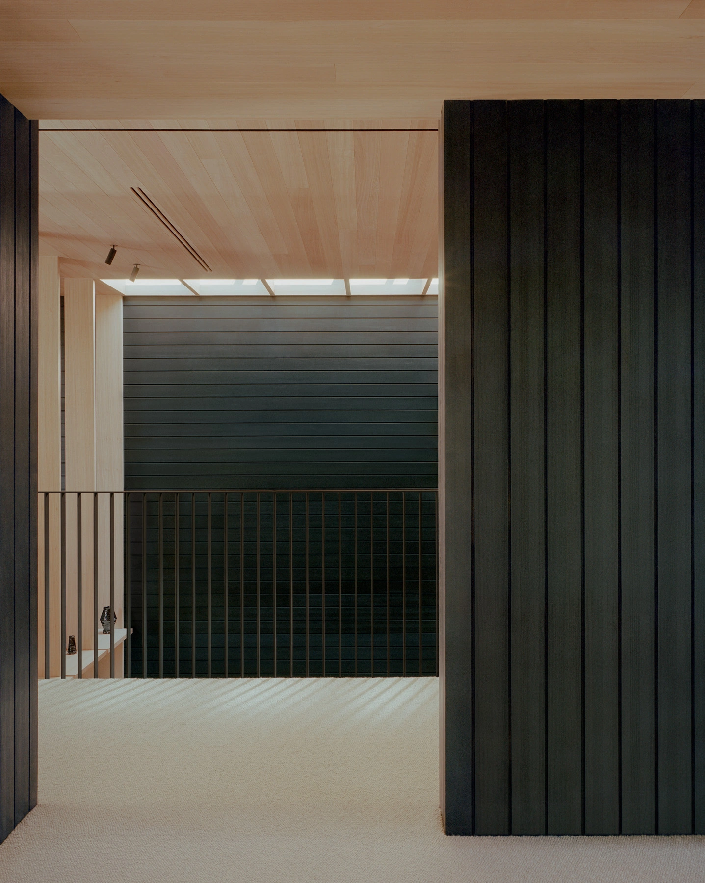 Echo House by Parabolica — The entry threshold frames a dual-material interior composition: charcoal horizontal timber slats form a continuous wall plane anchoring the far space,...