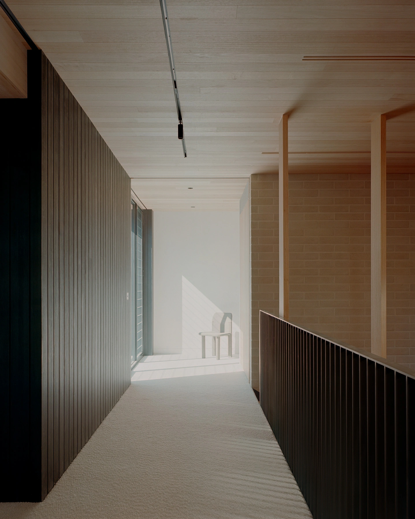 Echo House by Parabolica — A linear corridor extends toward natural light, framed by contrasting materiality: charcoal horizontal timber slats form a continuous wall plane on the...