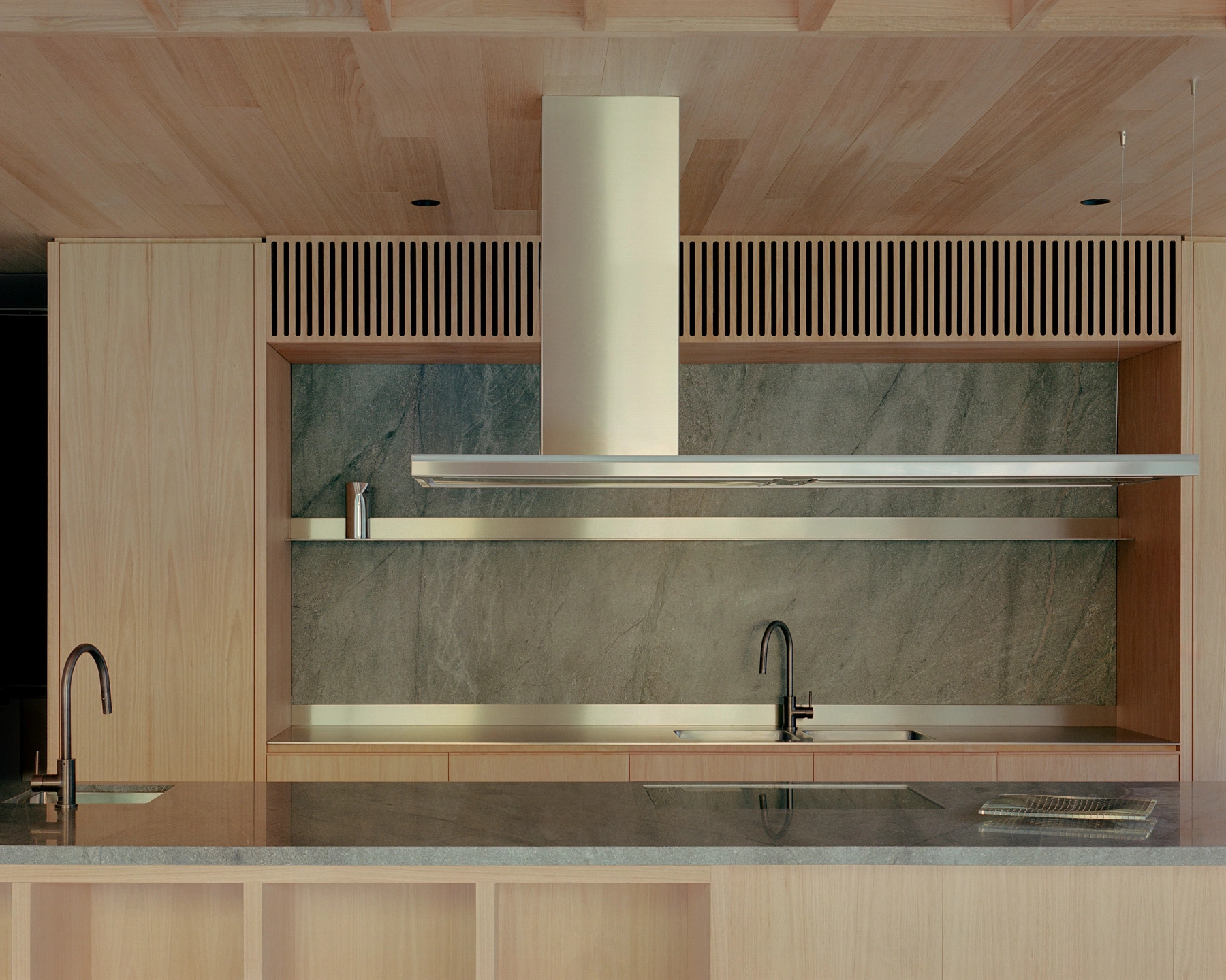 Echo House by Parabolica — The kitchen zone of Echo House features a minimalist composition anchored by a central cream-colored exhaust hood.