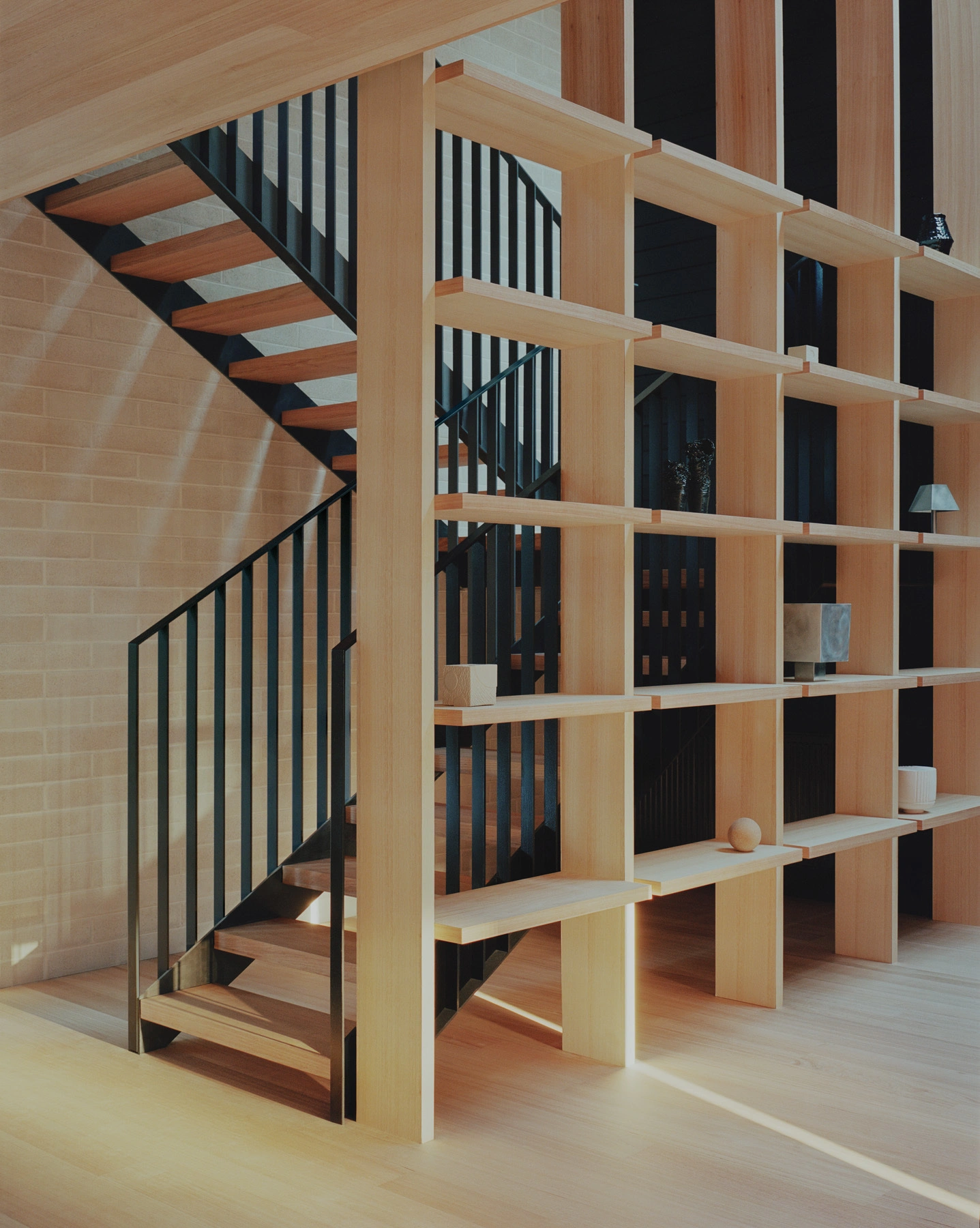 Echo House by Parabolica — A towering timber bookshelf in light pine dominates the ground floor, its grid of open compartments creating a rhythmic visual rhythm.