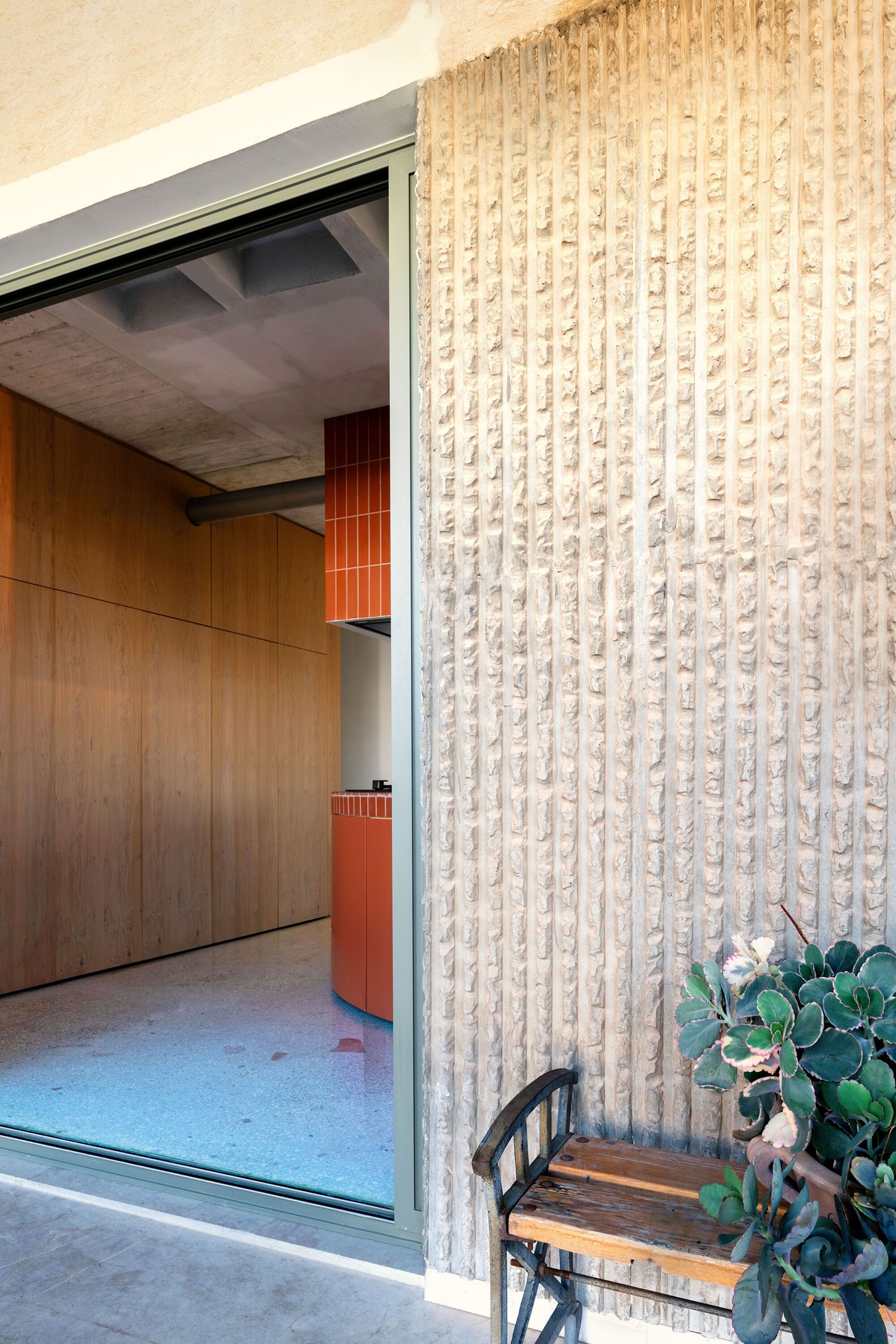 Three Object Apartment by DeMachinas + Elina Loukou — The pivoting cross mechanism is glimpsed through the threshold, its vertical terracotta tile wrapping appearing as a sculptural volume dividing interior space.