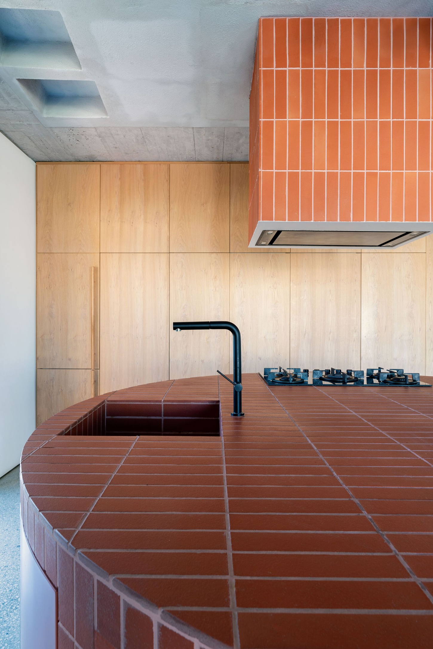 Three Object Apartment by DeMachinas + Elina Loukou — The Three Object Apartment's defining circular island occupies the spatial center, its perimeter wrapped in vertically-stacked terracotta tile that echoes...