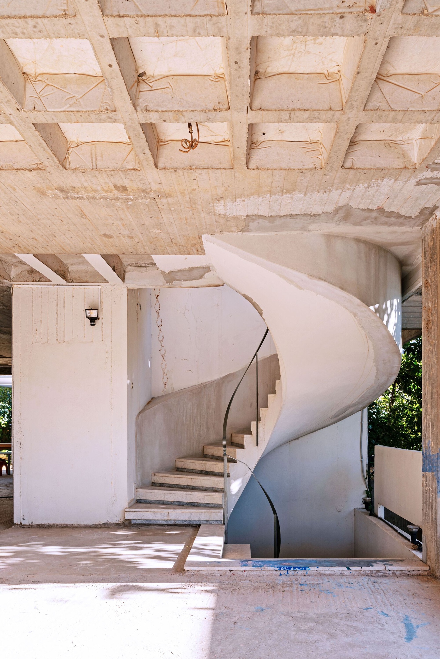 Three Object Apartment by DeMachinas + Elina Loukou — A spiral staircase dominates this under-construction interior, its curved concrete form wrapping counterclockwise beneath an exposed waffle ceiling.