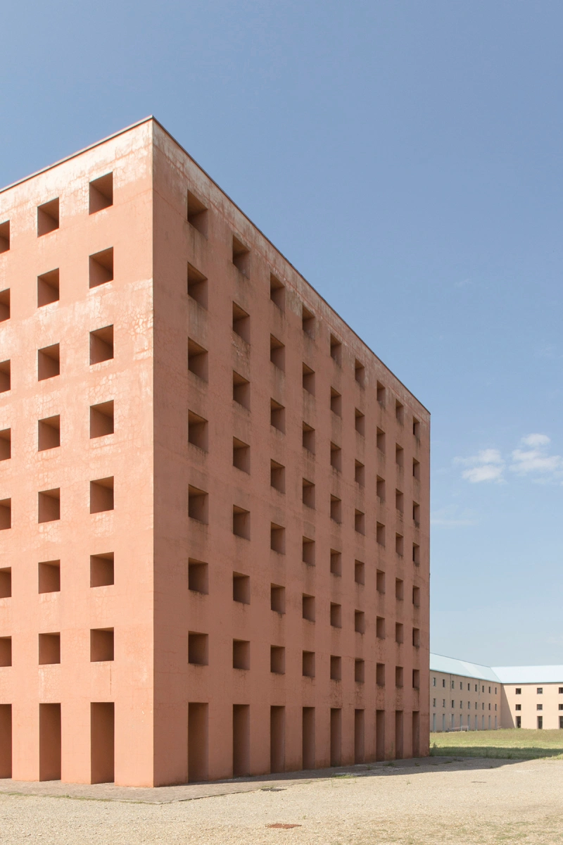 San Cataldo Cemetery by Aldo Rossi — A terracotta brick facade organized by a regular grid of square voids that penetrate the entire surface, creating a rhythmic pattern across the five-story...