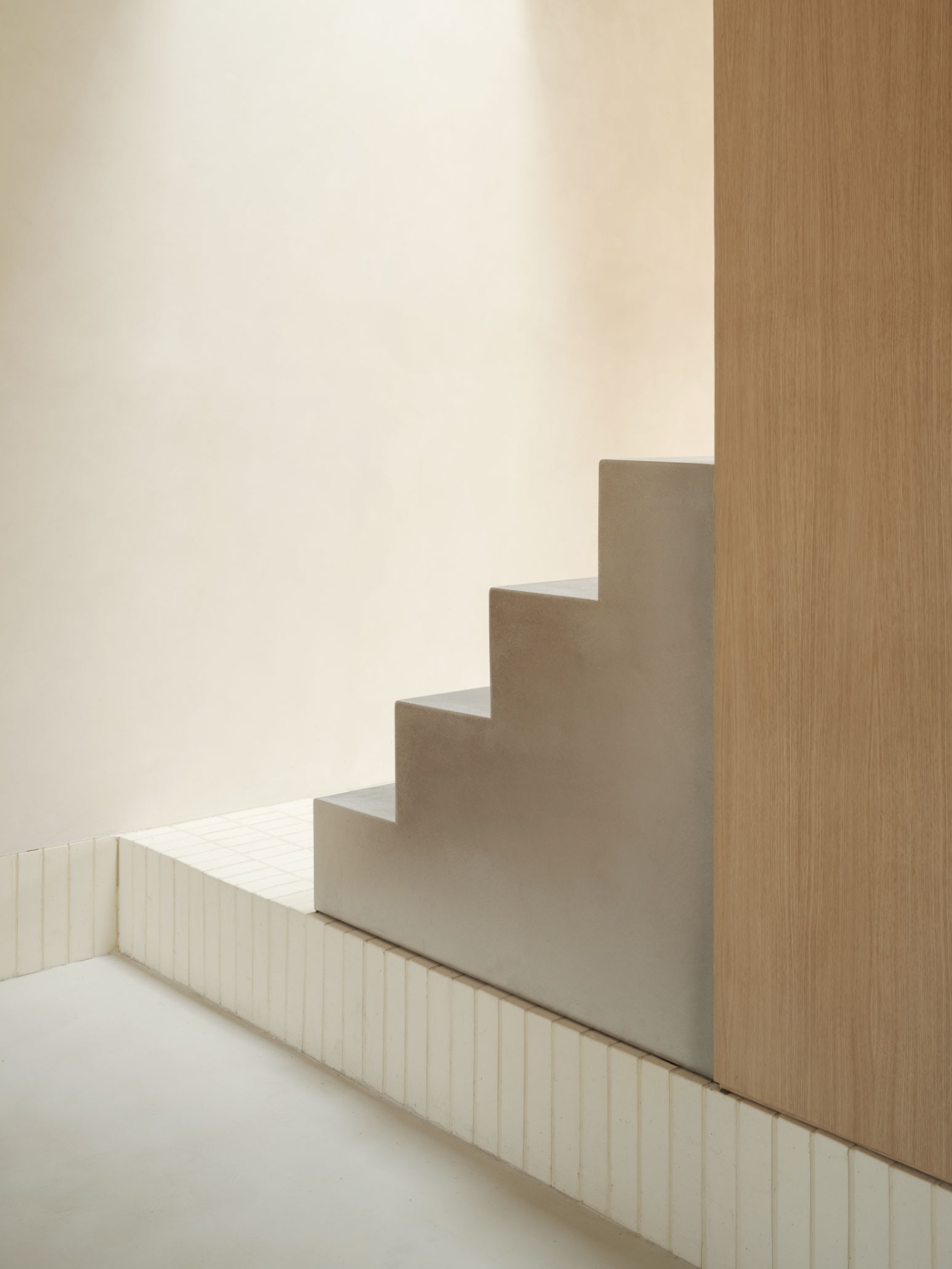 Casa SO by Studio DIIR — A stepped plaster form rises against timber paneling in this compressed domestic passage, its geometric profile casting precise shadows across pale walls.