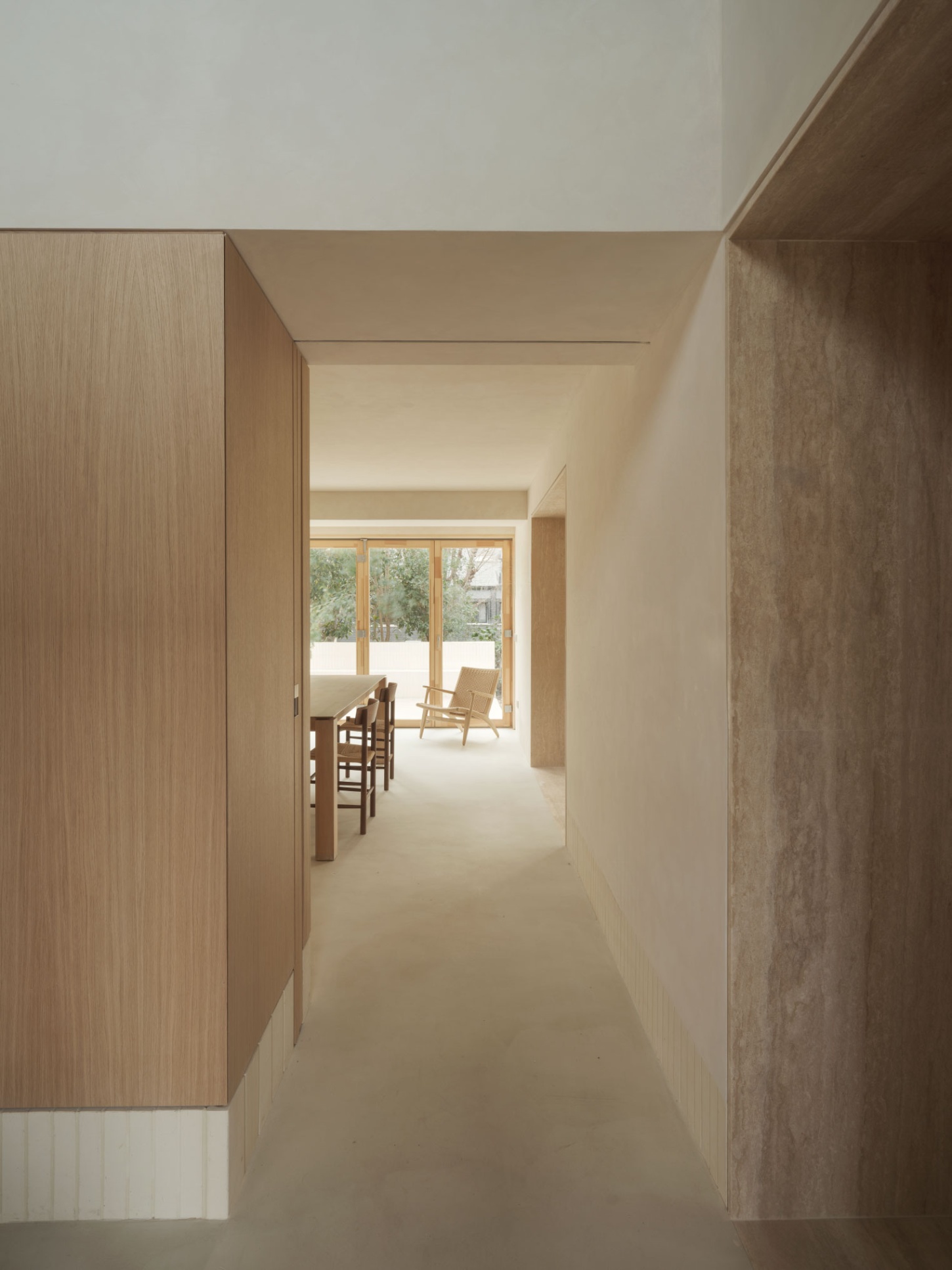 Casa SO by Studio DIIR — A narrow timber-lined passage stretches toward a sun-flooded living space, its compression deliberately proportioned to heighten the spatial release beyond.