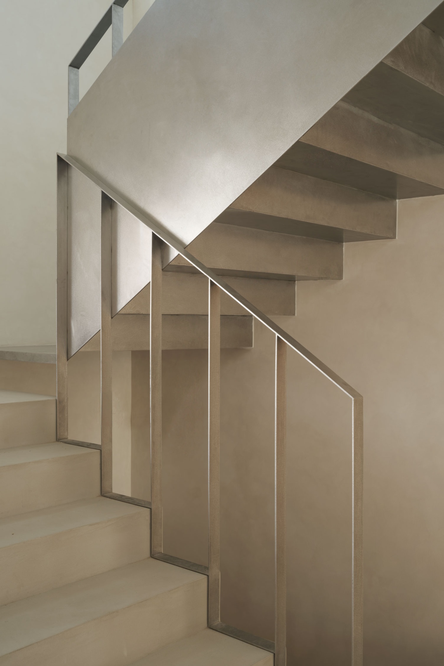 Casa SO by Studio DIIR — A cantilever stair descends through compressed vertical space, its timber-framed treads casting sharp shadows against pale plaster walls.