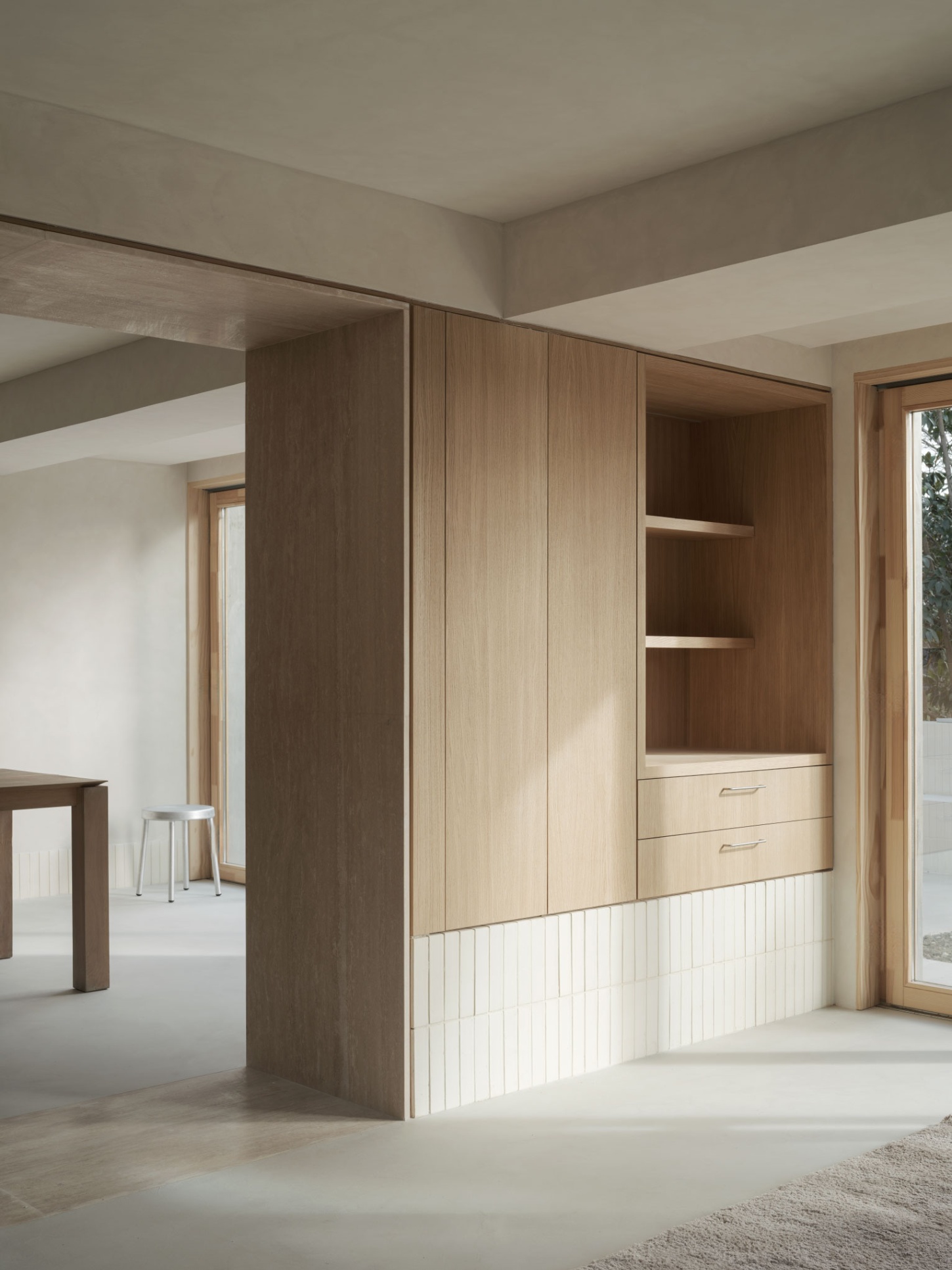 Casa SO by Studio DIIR — A timber-clad storage wall divides the domestic interior, its warm wood grain interrupted by two horizontal drawers with recessed metal handles positioned...