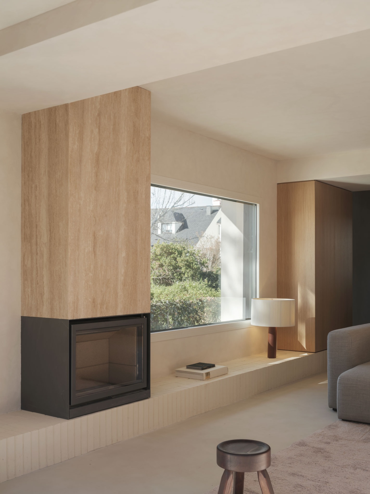 Casa SO by Studio DIIR — A timber-clad fireplace wall extends vertically from a dark steel hearth base, creating a monolithic wood panel that frames the interior threshold.